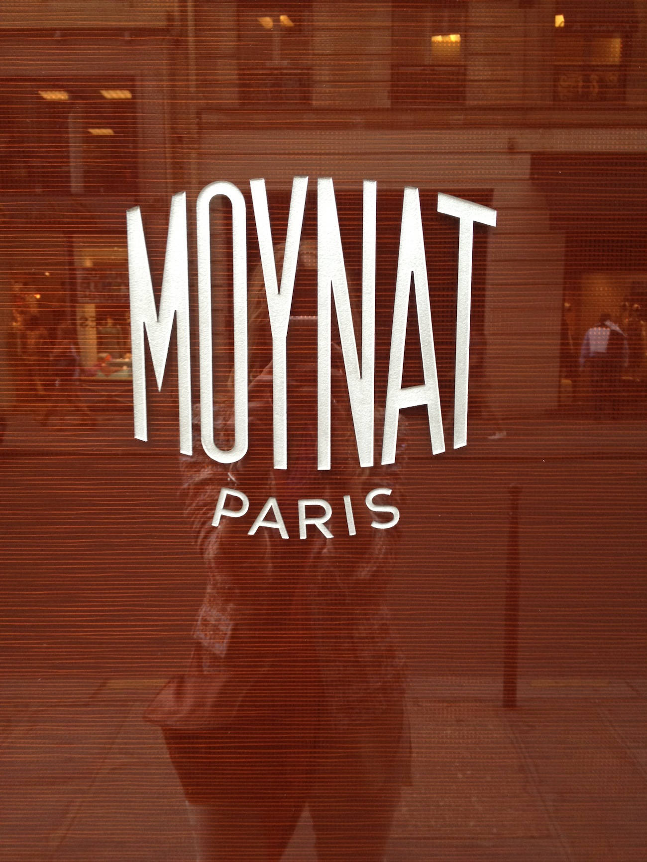 Moynat巴黎標誌 — 無可辨識的精緻 壁紙 — 一個人的倒影和「MOYNAT PARIS」標誌在有色玻璃商店櫥窗上可見，水平百葉窗投射出條紋。