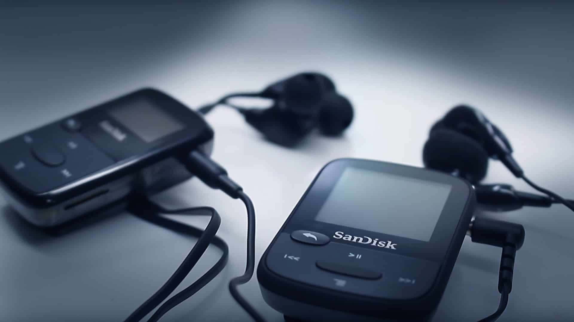 現代MP3播放器配耳機，背景為鮮豔色彩 壁紙 — 兩部黑色SanDisk MP3播放器連耳塞，在冷色燈光下放置於柔和的漸變表面上。
