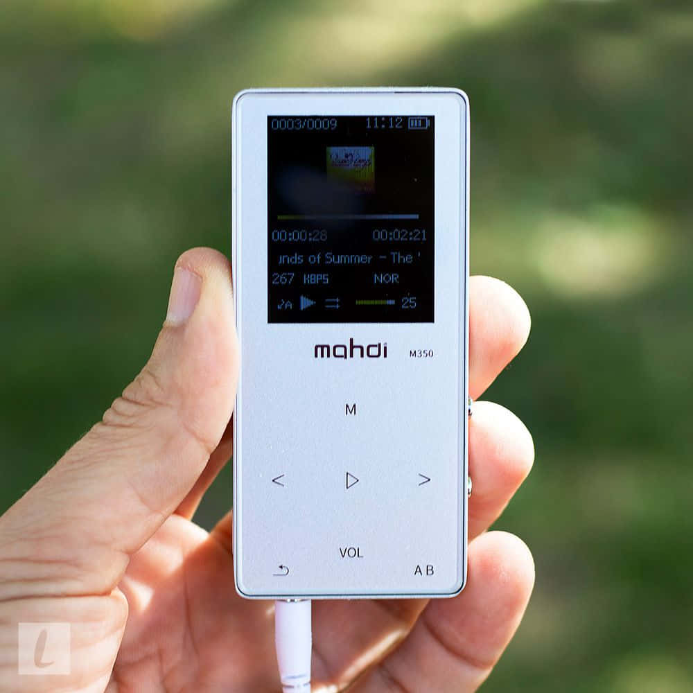 手持小型MP3播放器的人 壁紙 — 一隻手拿著銀色 Mahdi M350 MP3 播放器，在模糊的綠色戶外背景上顯示音樂播放。