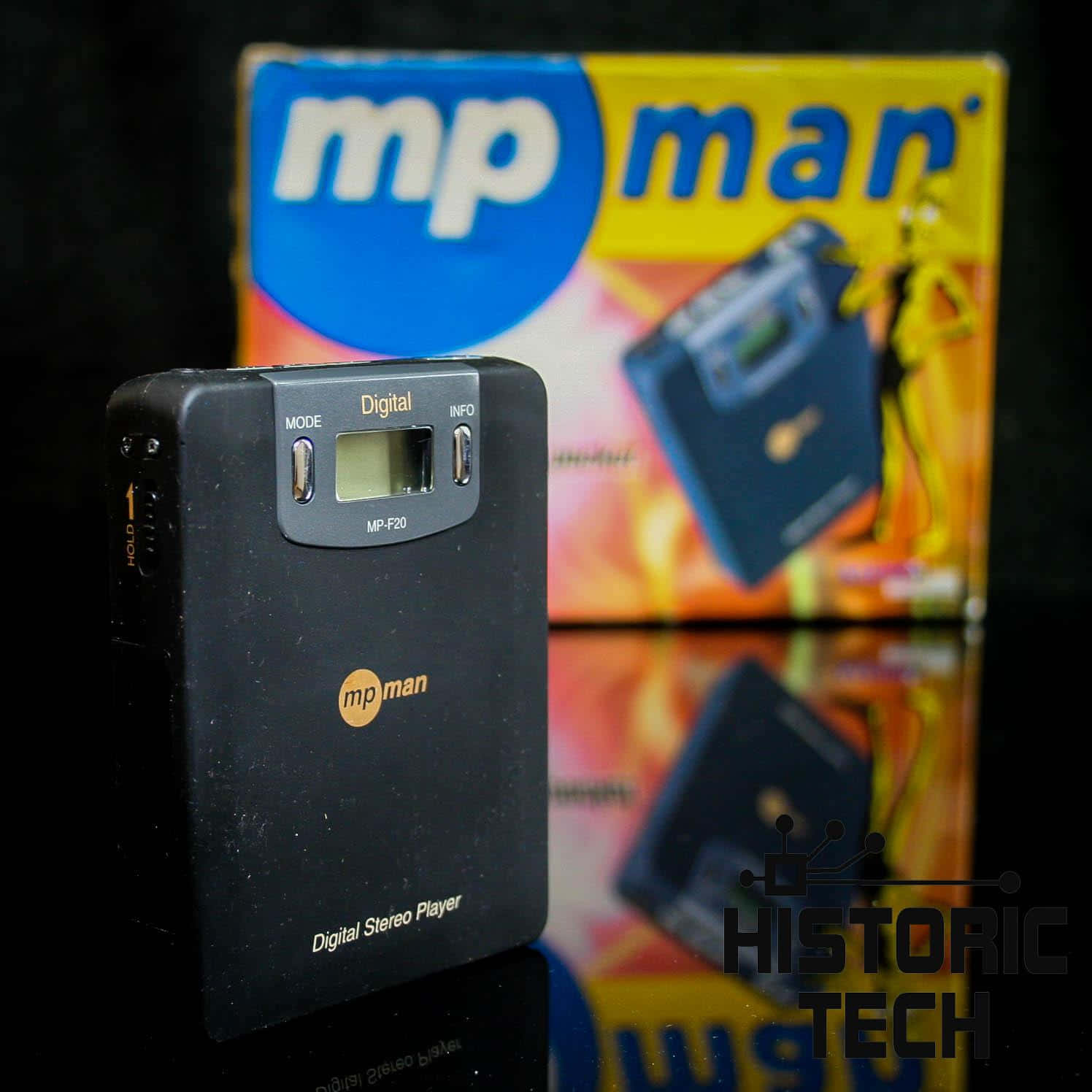 MPman MP3播放器（1998年首度問世） 壁紙 — 一個黑色mp man數碼立體聲播放器放在其彩色盒子前面，置於反光表面上。