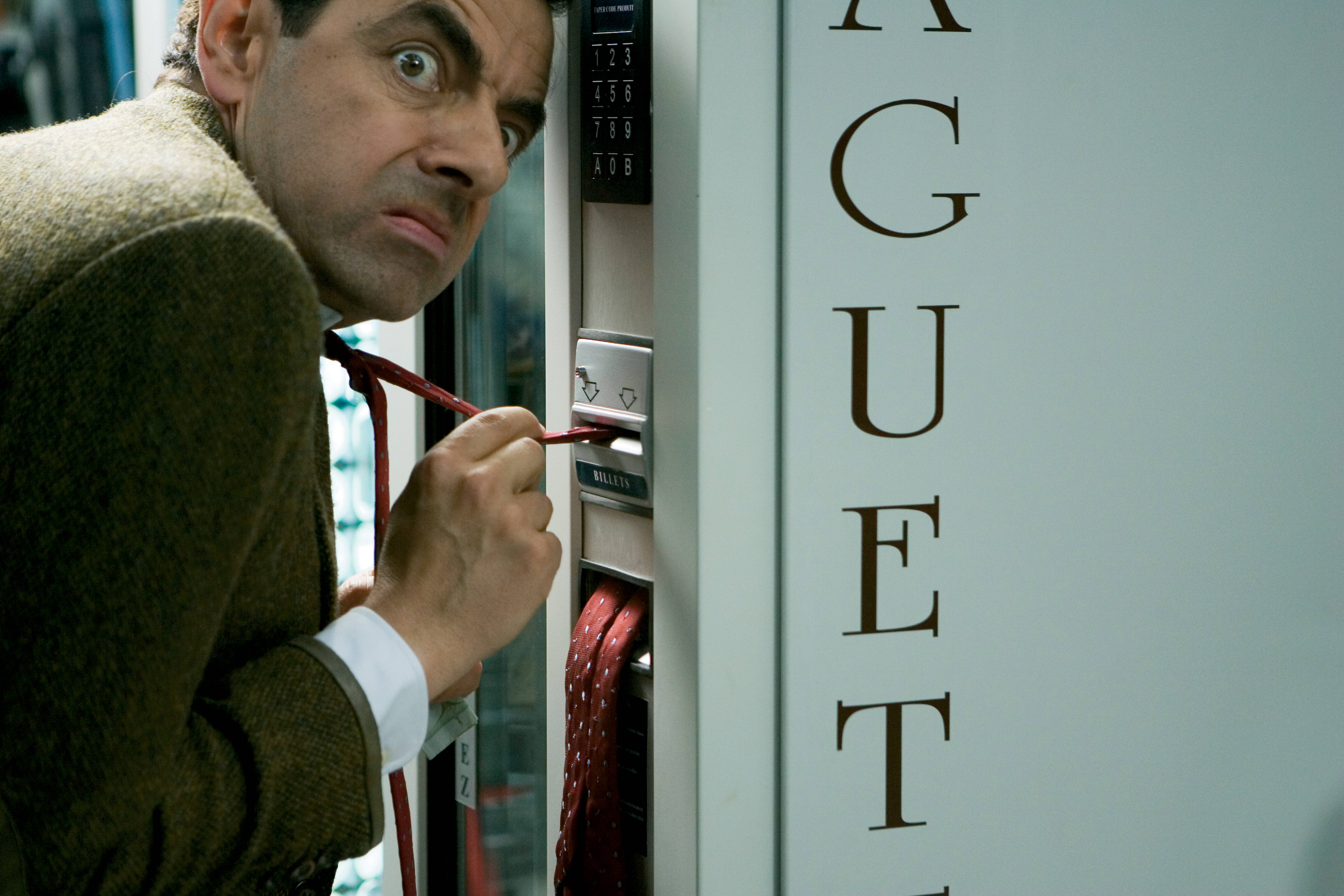 4K 桌布 壁紙 — Mr Bean 專注地凝視，同時嘗試用紅色領帶作為工具操作自動售賣機。