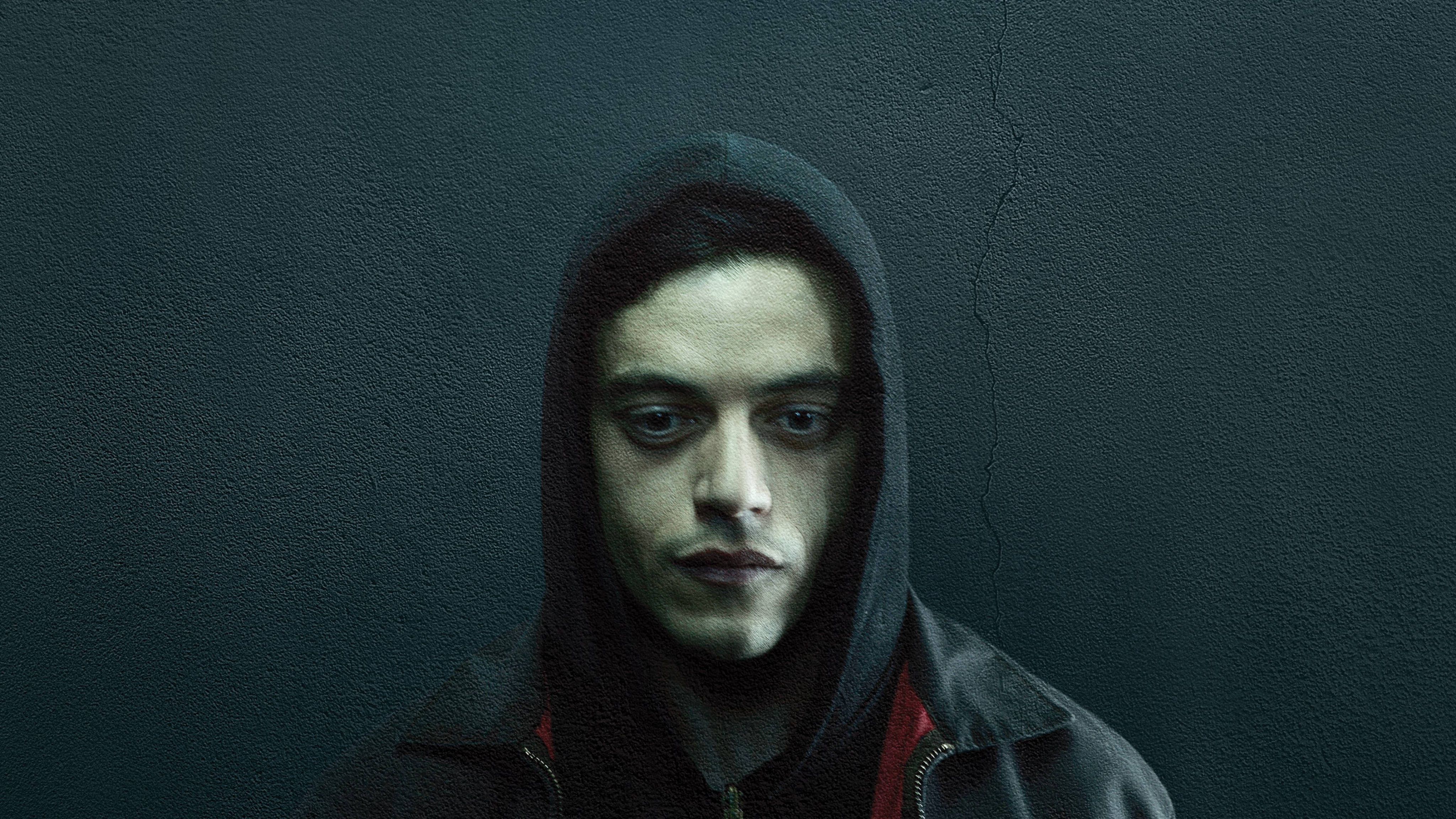《Mr. Robot》艾略特·格雷背景 壁紙 — 一個穿著深色連帽衫的年輕男子在昏暗燈光下，對著裂開的藍綠色牆壁強烈凝視。