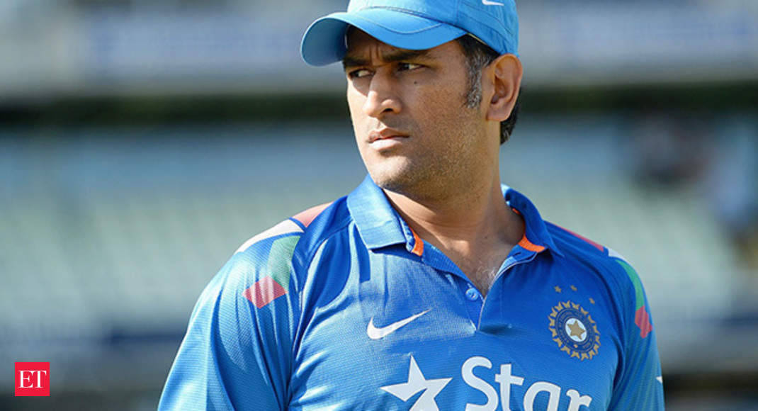 MS Dhoni 7 中景 壁紙 — 一位專注的印度板球運動員，身穿藍色制服和帽子，站在陽光普照的體育場上。