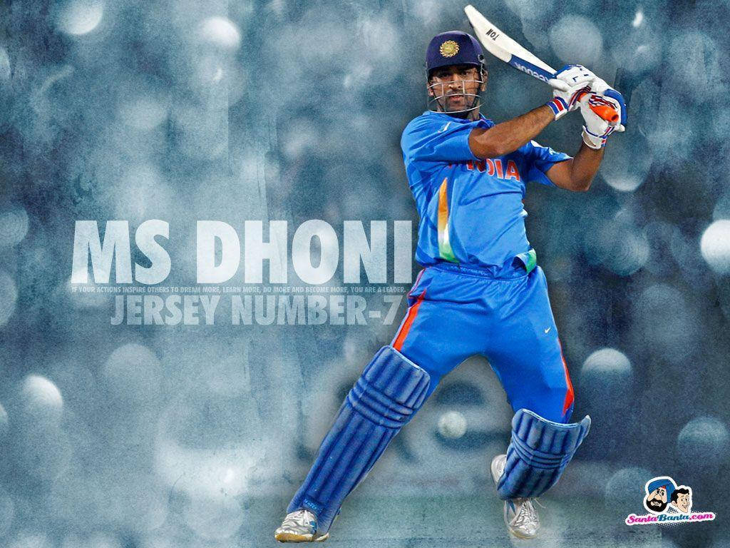 MS Dhoni七號球衣 壁紙 — 板球傳奇 MS Dhoni 身穿藍色印度隊服，在模糊的體育場背景和發光球體中揮棒。