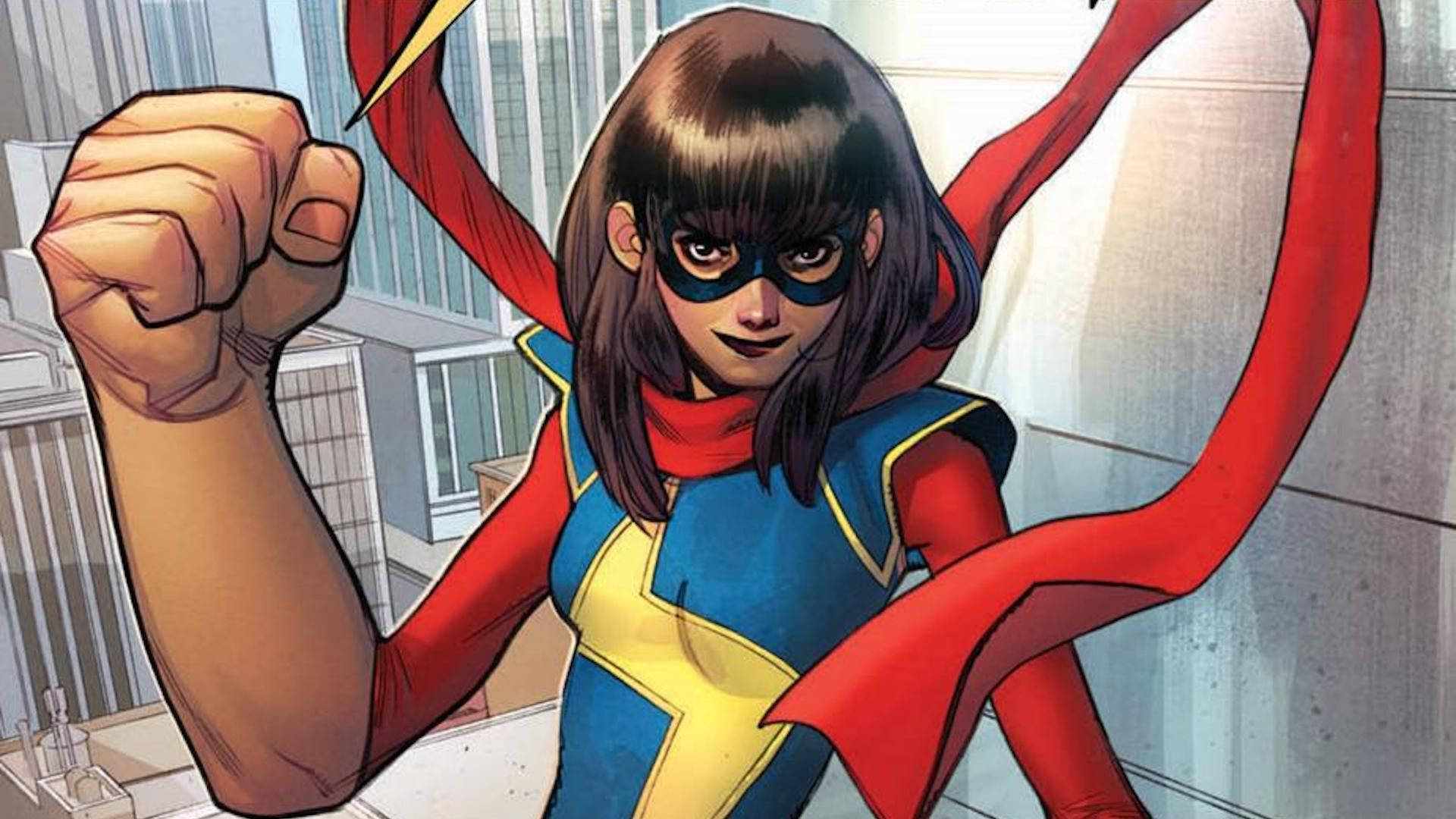 Ms Marvel 眼神冷峻 壁紙 — 一位自信的女超級英雄，身穿藍、紅、黃三色服裝，披著飄逸的斗篷，在城市天際線前英勇站立。