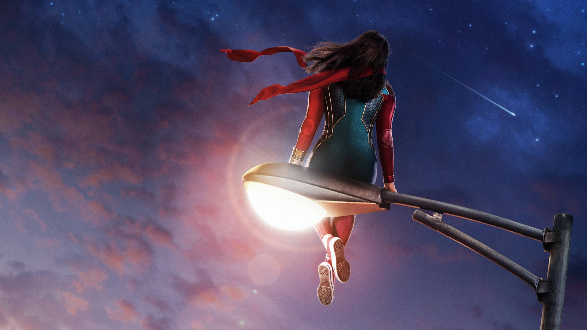 Ms Marvel 與流星 壁紙 — 驚奇隊長棲息在發光的街燈頂上，背景是繁星點點的暮色天空，一顆流星劃過。