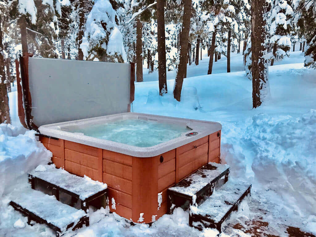  壁紙 — 一個木製熱水浴缸隱藏在雪地森林中，溫暖的水中升起蒸氣，周圍是白雪覆蓋的松樹。
