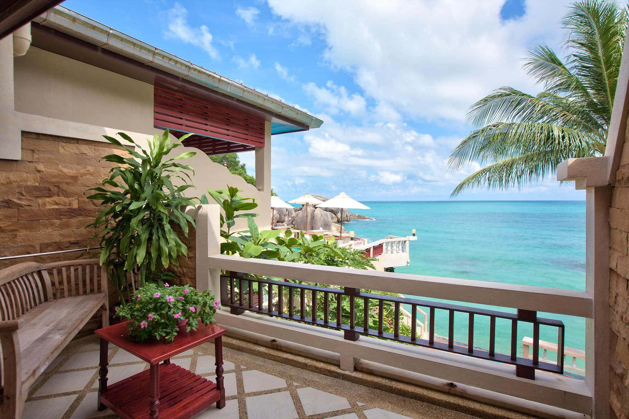 Beach Resort 桌布 壁紙 — 木製陽台俯瞰著碧藍色的海洋，有棕櫚樹和白色遮陽傘，在明亮的藍天下。
