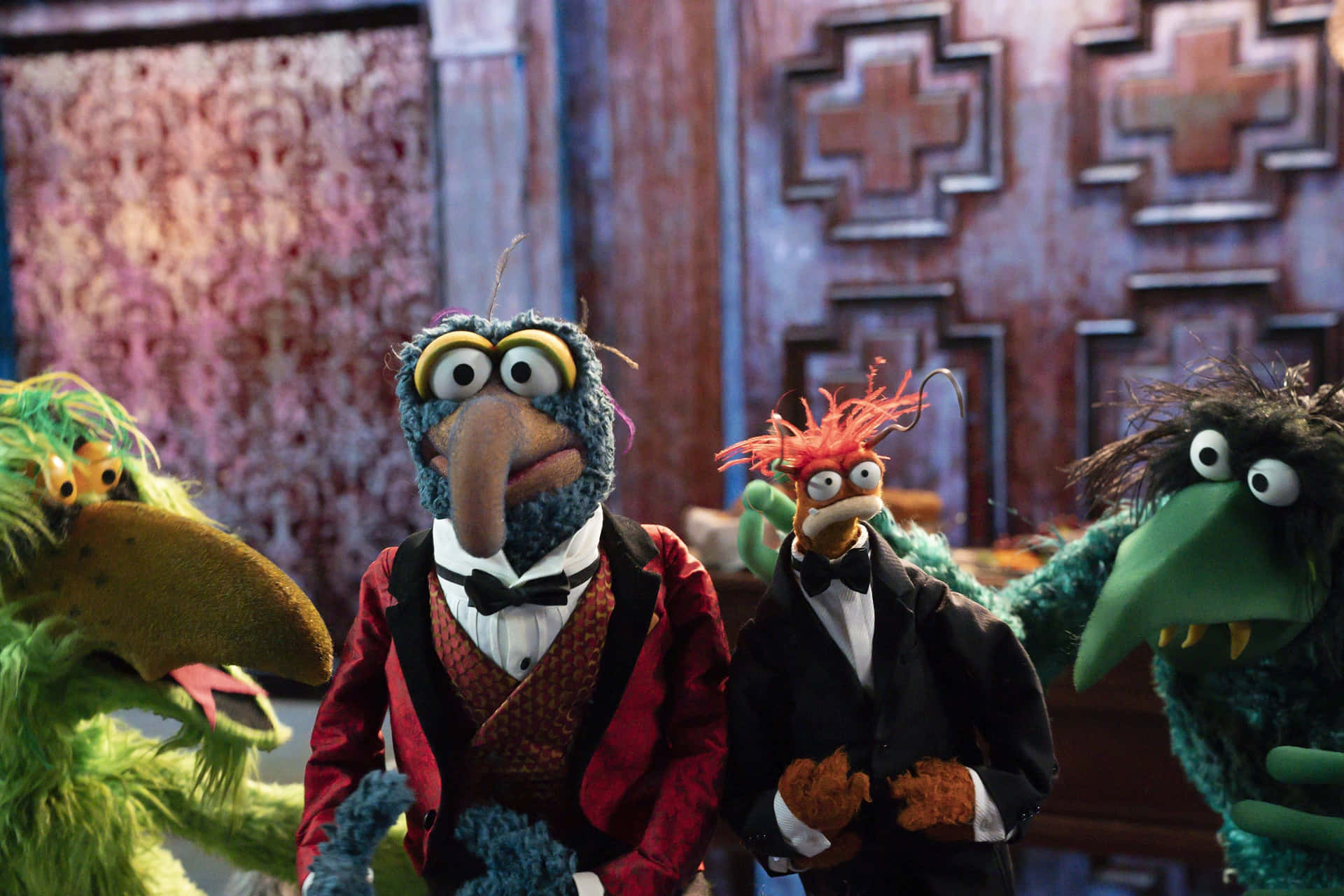 Muppets Gonzo 及朋友出席活動 壁紙 — 四個色彩繽紛的Muppet角色身穿正裝，在圖案牆紙和華麗木門前擺姿勢。