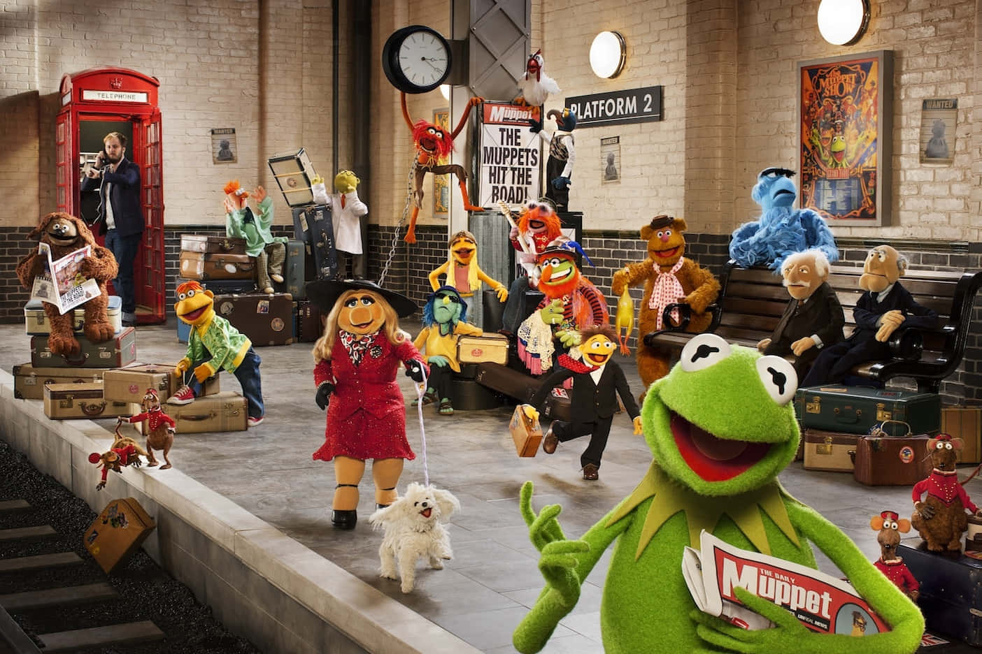  壁紙 — Muppets 角色在火車站月台上熙熙攘攘，背景有行李和一個紅色電話亭。
