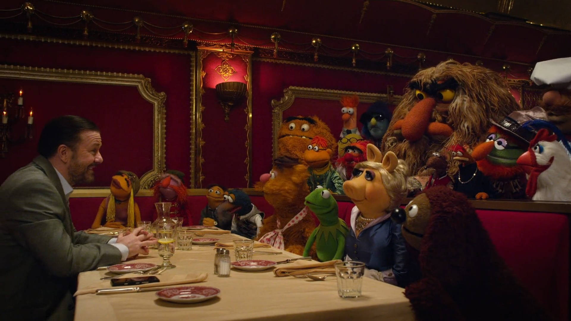 男子在紅色天鵝絨餐廳卡座中與Muppets共進晚餐。