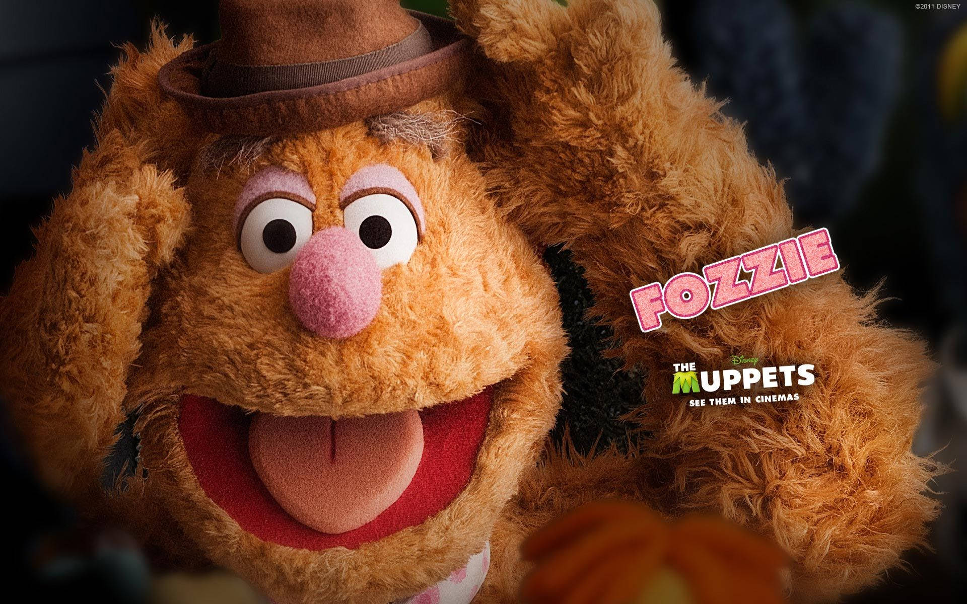 Muppets 的 Fozzie Bear 壁紙 — Fozzie Bear 嘅特寫，戴住啡色 fedora 帽，咧嘴大笑，伸脷，背景係深色。