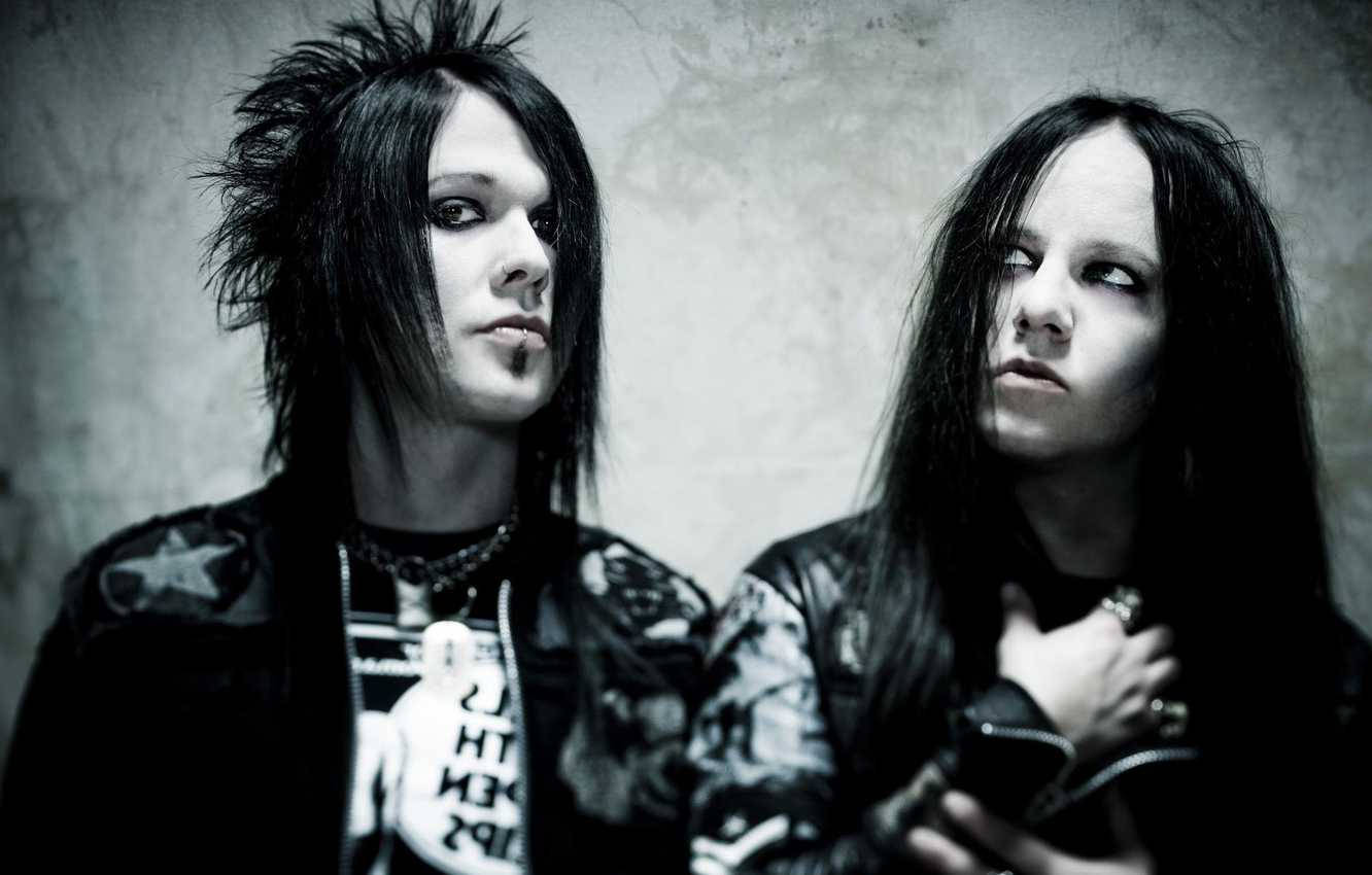 喬伊·喬迪森 Murderdolls 壁紙 — 兩位哥德音樂家，擁有刺蝟般的黑髮和深色妝容，在紋理灰色牆壁前強烈擺姿勢。
