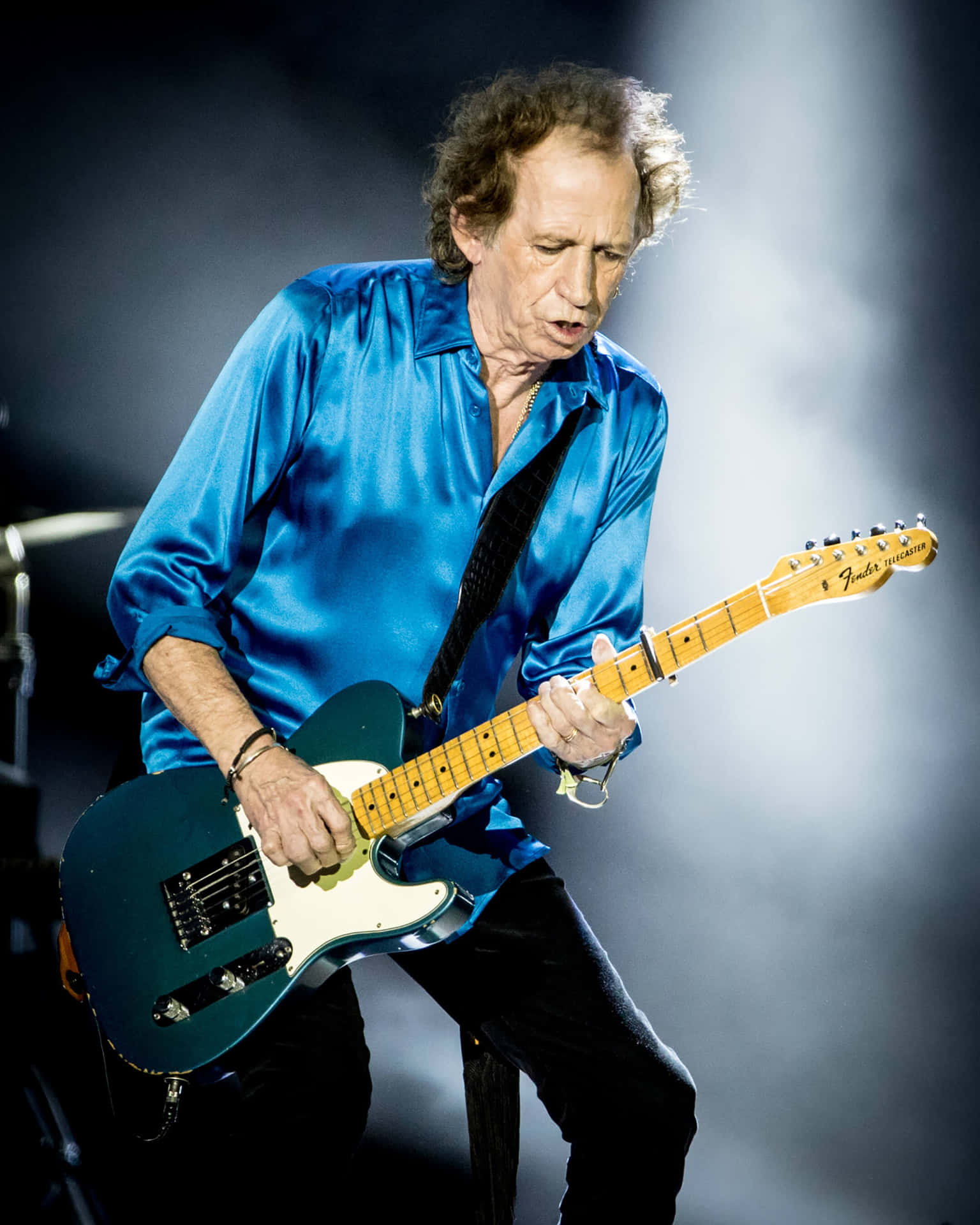  壁紙 — 一位身穿閃亮藍色襯衫的音樂家在舞台燈光下熱情地彈奏一支青綠色的Fender Telecaster。