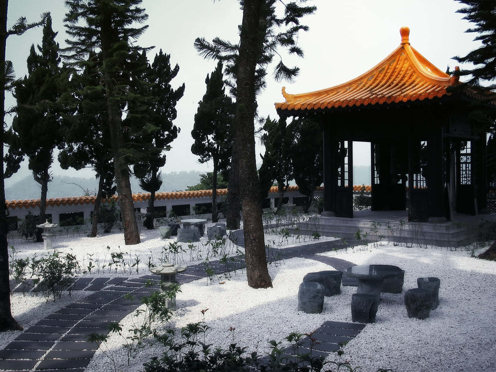mute 橙色寺廟 壁紙 — 一座傳統中式亭閣，橙色屋頂，矗立在高大樹木和白色碎石花園小徑之間。