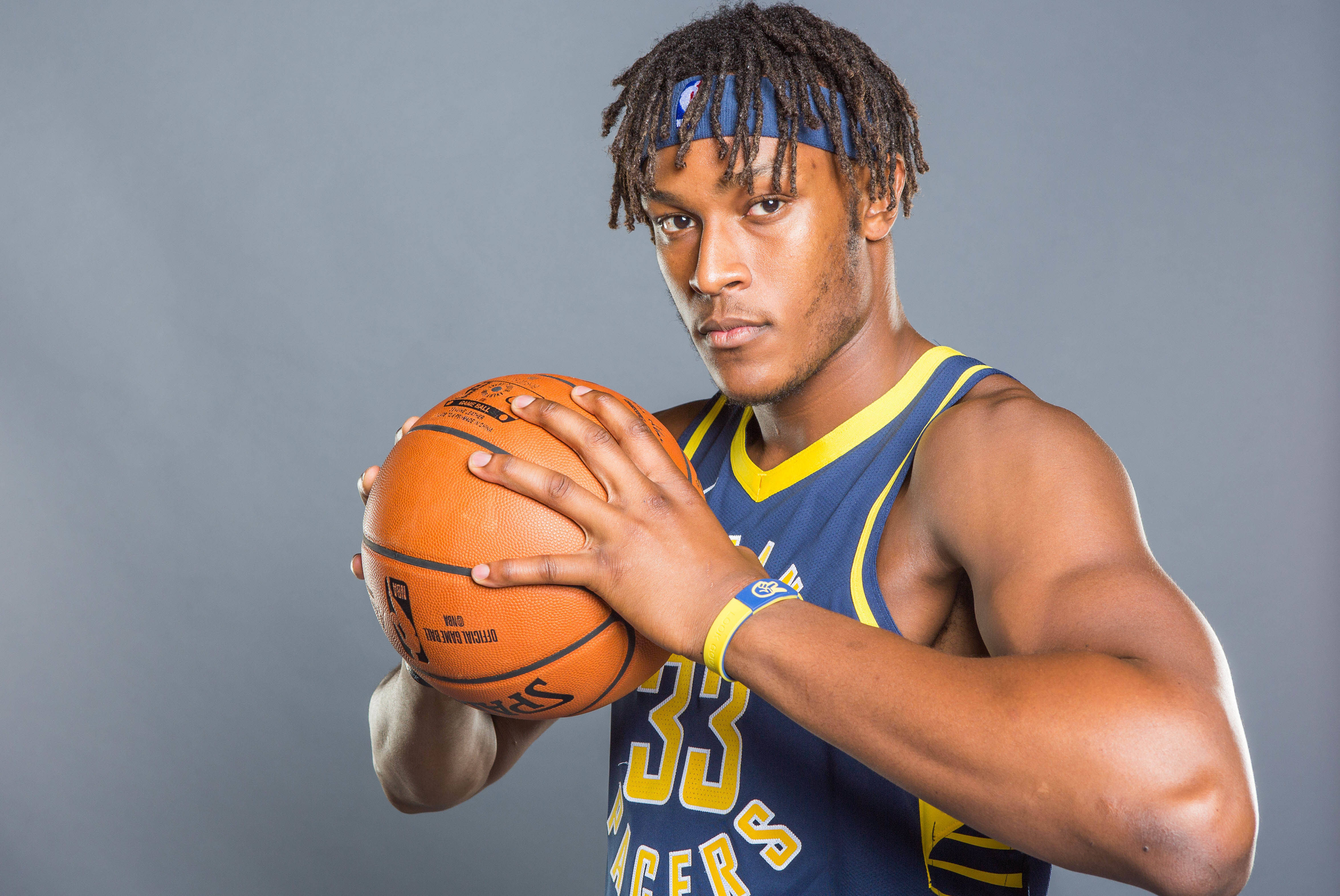 Myles Turner 籃球拍攝照 壁紙 — 一位專注的籃球運動員，身穿藍黃色球衣，在純灰色工作室背景前拿著一個橙色籃球。
