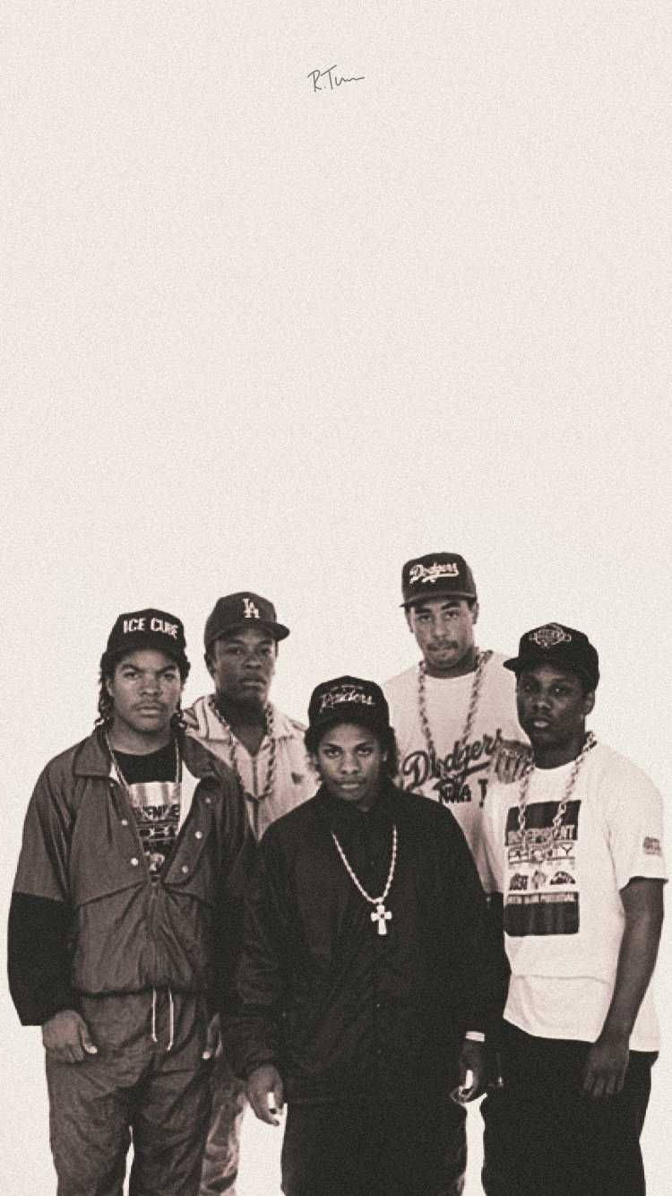N.W.A. 90年代嘻哈樂團經典群像 壁紙 — 五個戴著帽子和鏈條的男人在素色背景前自信地擺姿勢，一張復古黑白照片。