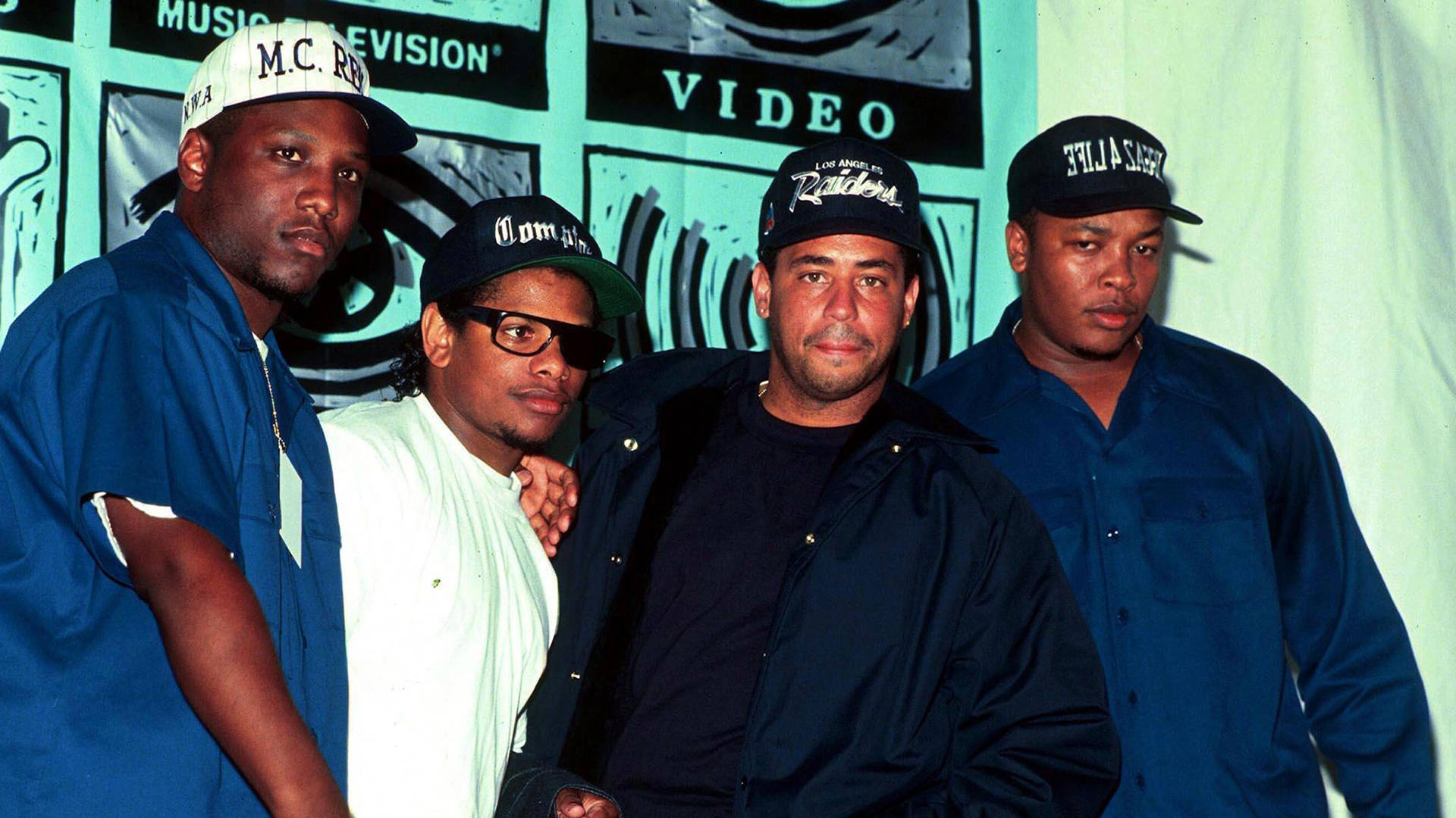 N.W.A.出席1991年MTV音樂錄影帶大獎 壁紙 — 四個戴帽、身穿休閒服的男人在藍綠色Music Television Video背景前自信地擺姿勢。