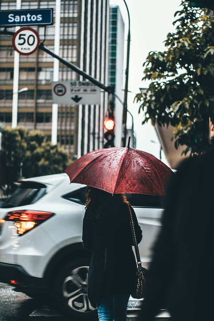 Downtown Girl Aesthetic 桌布 壁紙 — 一個拿著紅色雨傘的人走過一條有高樓大廈和閃爍交通燈的雨中城市街道。