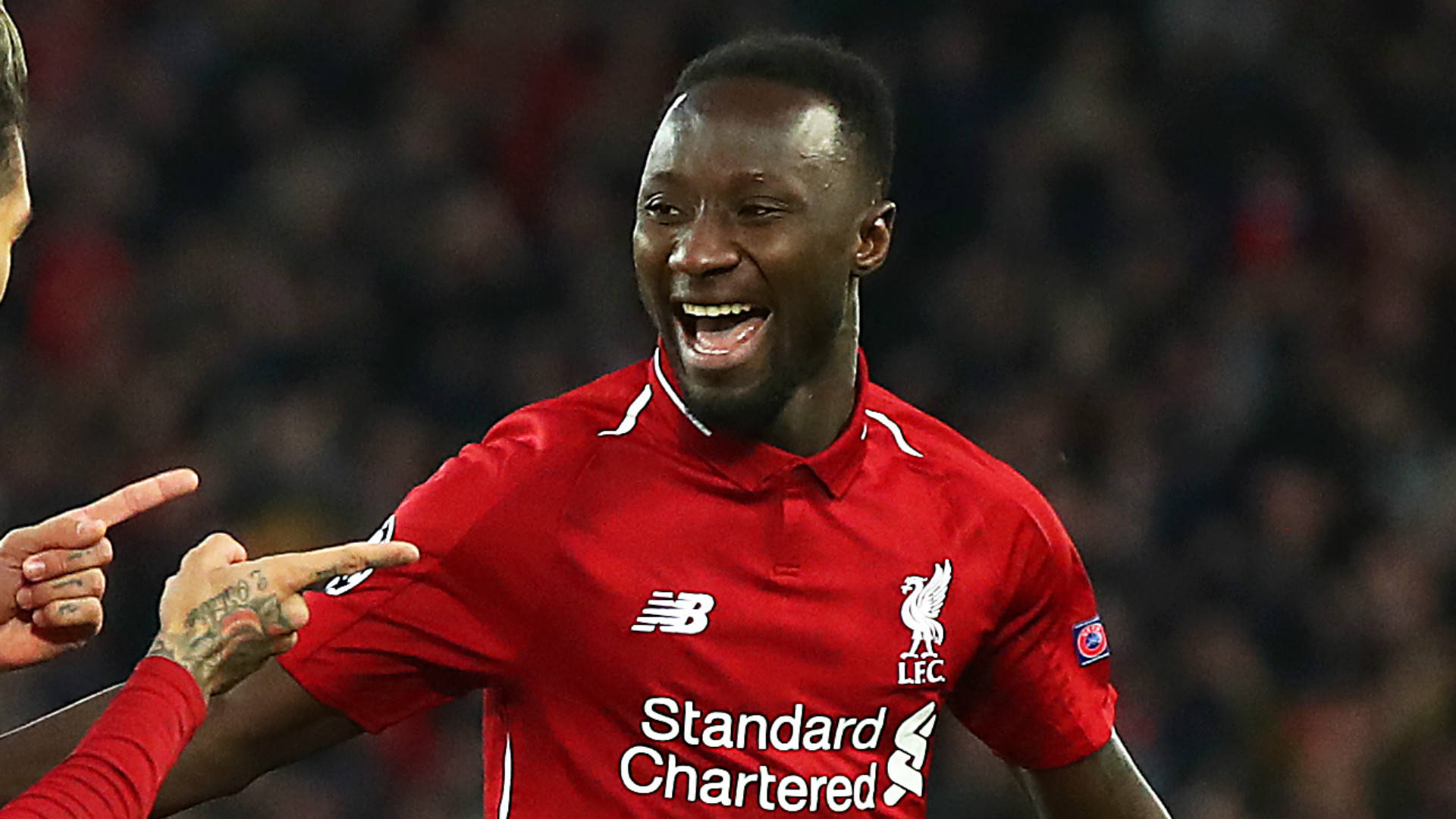 Naby Keita 被隊友調侃 壁紙 — 一位身穿紅色球衣的利物浦足球員在球場燈光下與隊友慶祝。