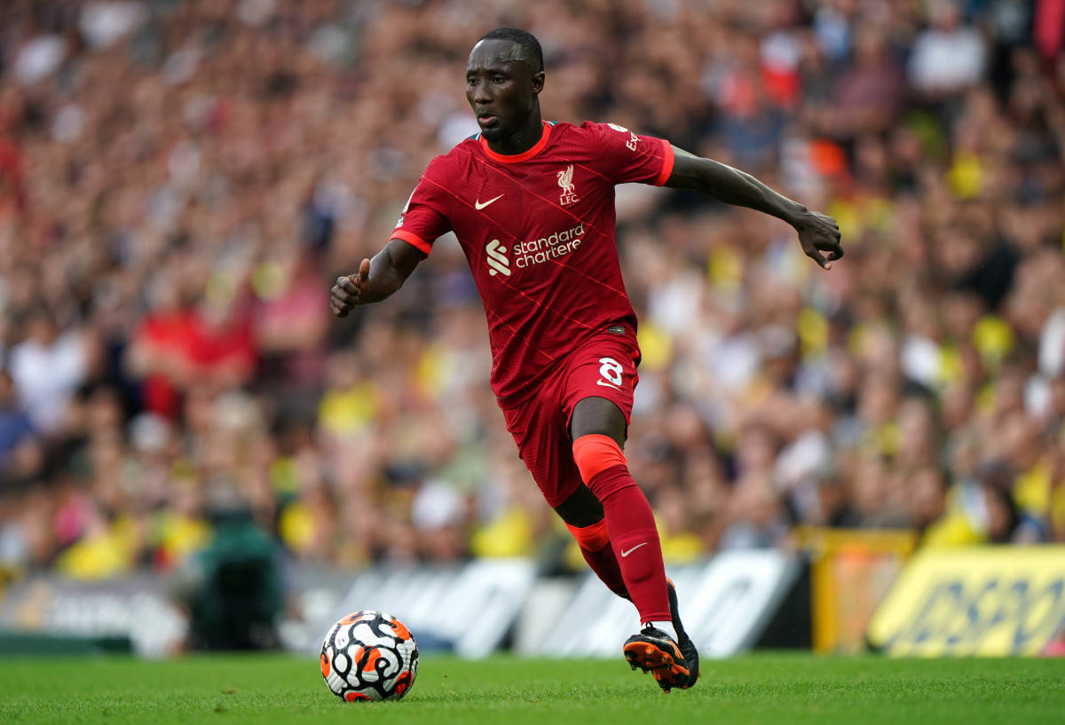 Naby Keita 配色足球 壁紙 — 一名身穿紅色球衣的利物浦足球員在陽光普照的球場上盤球，背景有模糊的人群。