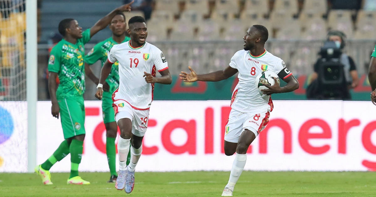 Naby Keita 高五慶功 壁紙 — 兩名身穿白色球衣的歡欣足球運動員在充滿活力的綠色球場上慶祝入球，球場燈光在上方閃耀。