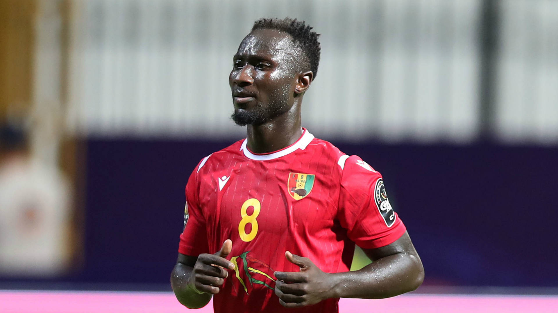 Naby Keita 黃色8號 壁紙 — 一名汗流浹背的加納足球員身穿紅色8號球衣，在球場燈光下的夜間比賽中激烈地做手勢。