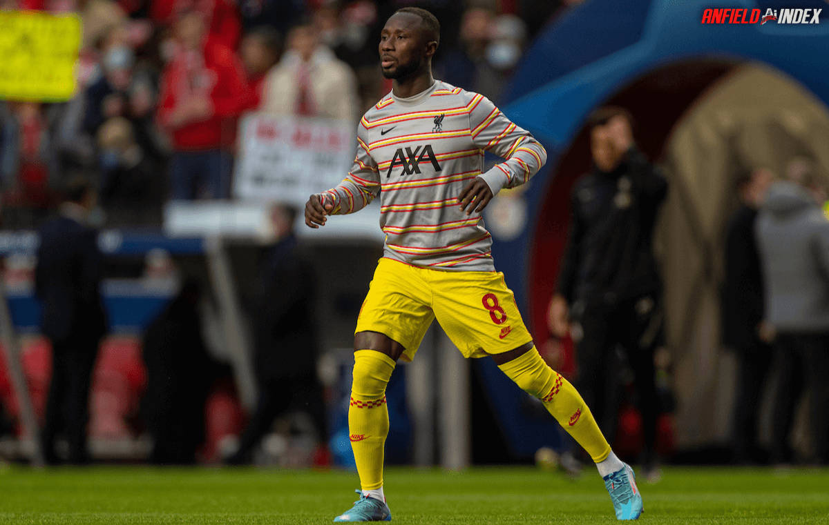 Naby Keita 黃色短褲 壁紙 — 一名身穿條紋球衣和黃色短褲的足球運動員在綠色球場上奔跑，背景是模糊的體育場觀眾。