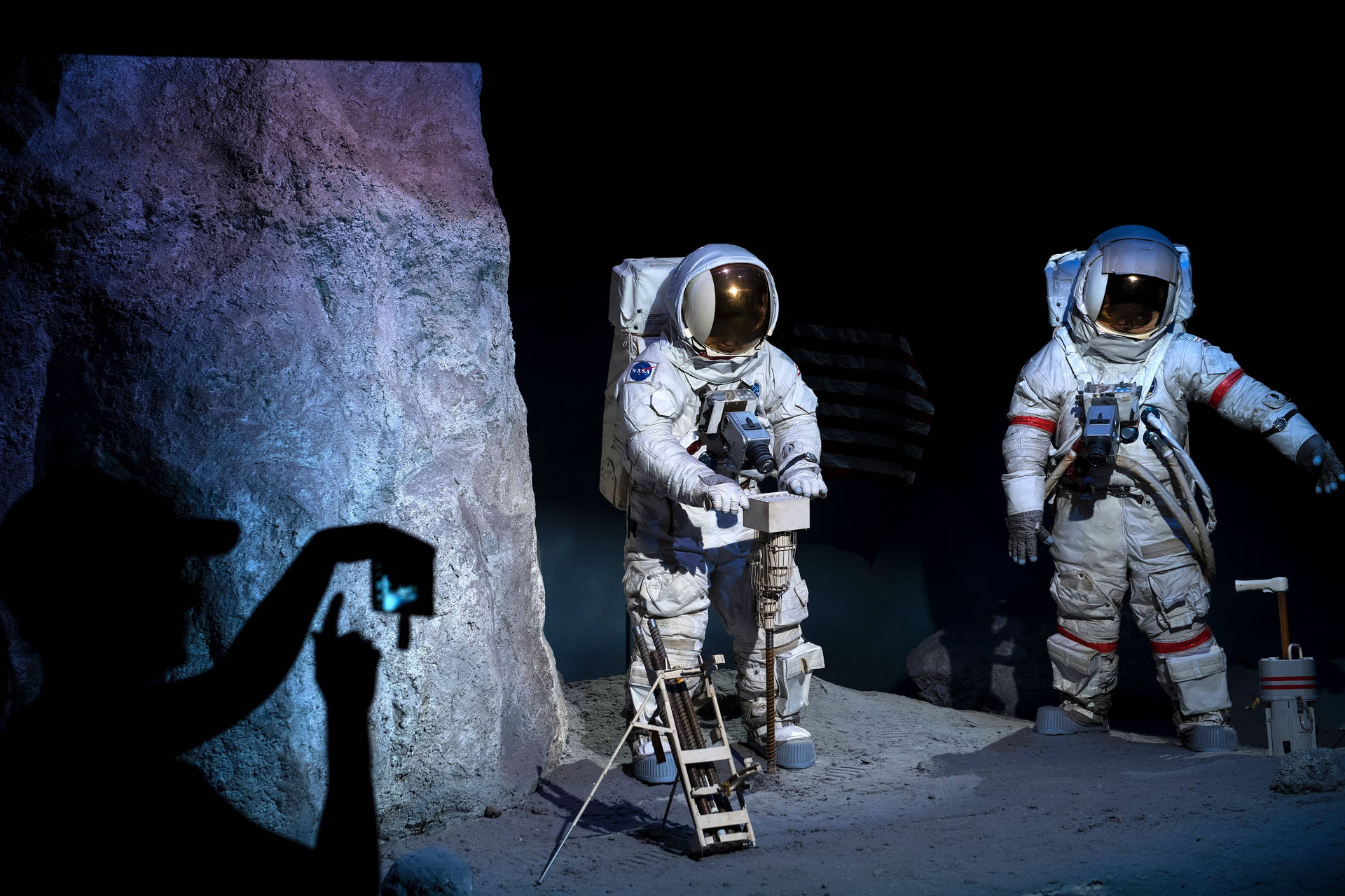 剪影人物在月球般的地形上拍攝兩名太空人形象。 — Nasa GIF 壁紙