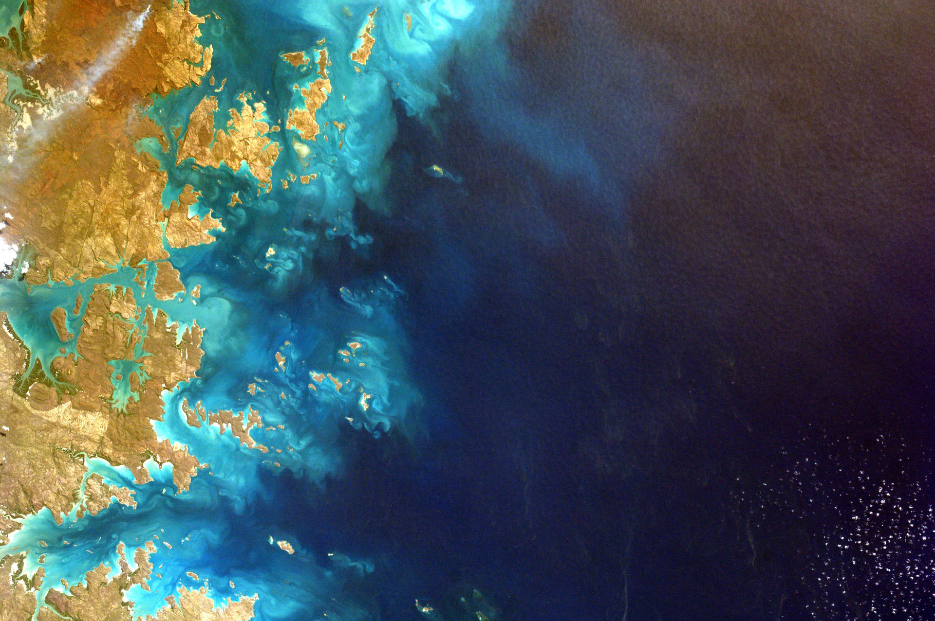 衛星視角的海岸線，金色陸地與藍綠色海洋交匯深藍色大海。