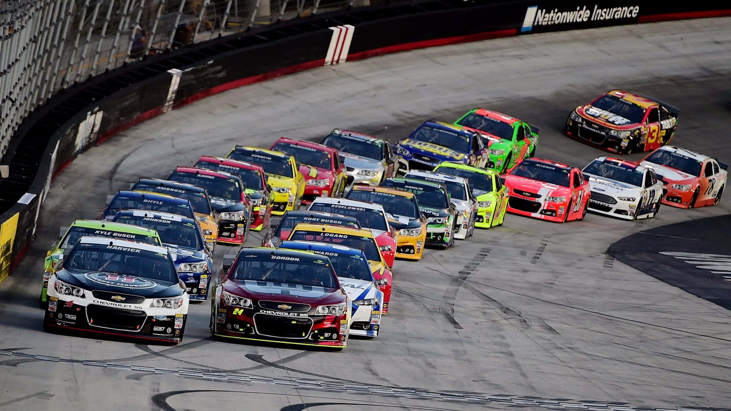NASCAR車手疾馳賽道 壁紙 — 一組色彩鮮豔的NASCAR賽車緊密地擠在一起，在賽道上高速過彎。