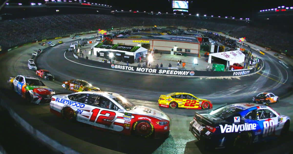 衝向終點線——NASCAR賽事的興奮 壁紙 — 夜間NASCAR賽車在布里斯托爾賽車場的體育場燈光下，在明亮照明的橢圓形賽道上呼嘯而過。