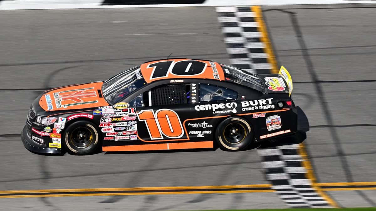 NASCAR賽車的刺激感 壁紙 — 一輛黑色和橙色的10號賽車在陽光明媚的賽道上越過格仔旗終點線。