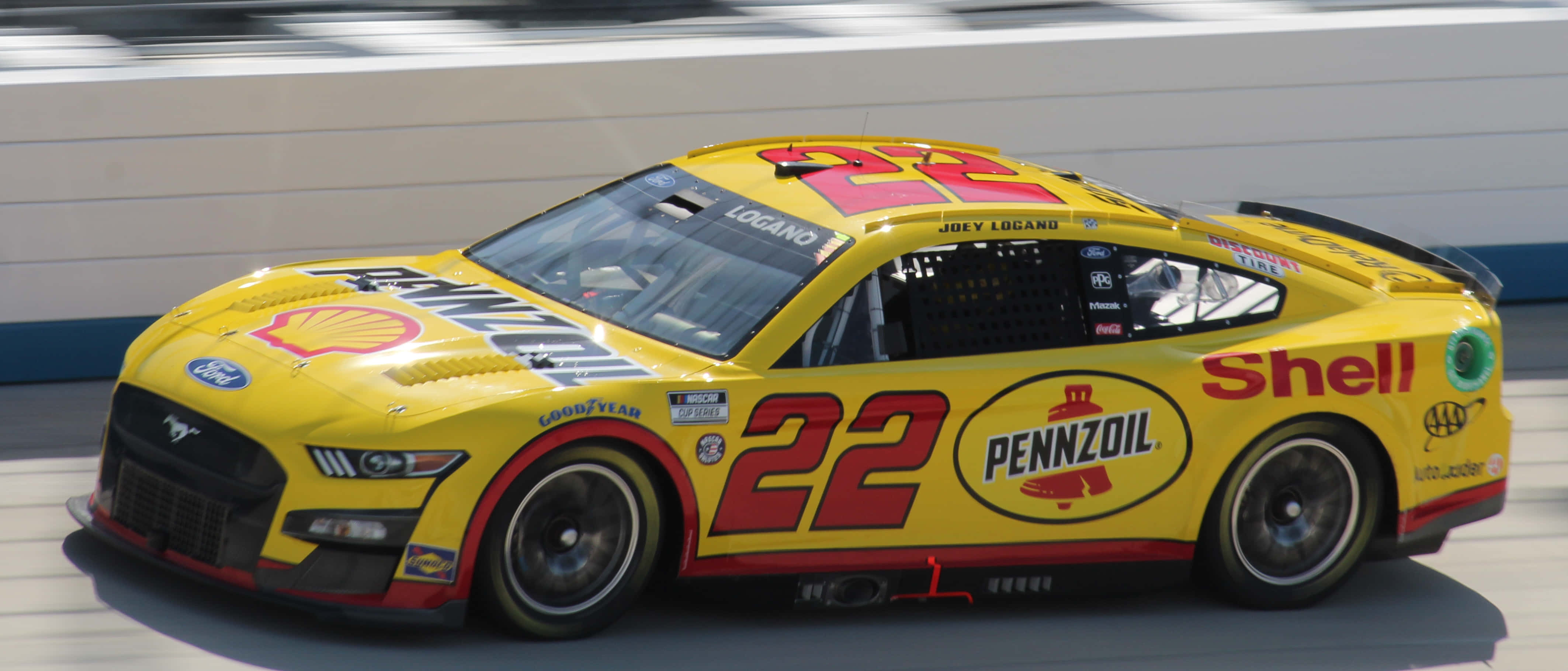 NASCAR 賽事現場 360° 觀眾全景 壁紙 — 一輛亮黃色的NASCAR賽車，編號22，在晴朗的白天沿著賽道飛馳。