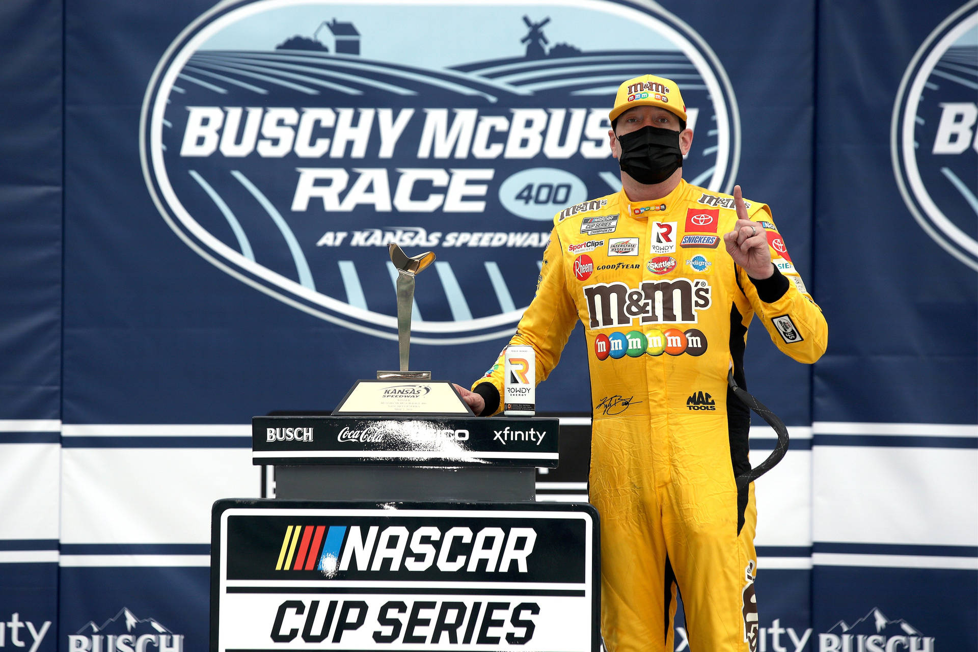 身穿黃色賽車服的NASCAR車手在堪薩斯賽道的頒獎台上高舉獎盃。