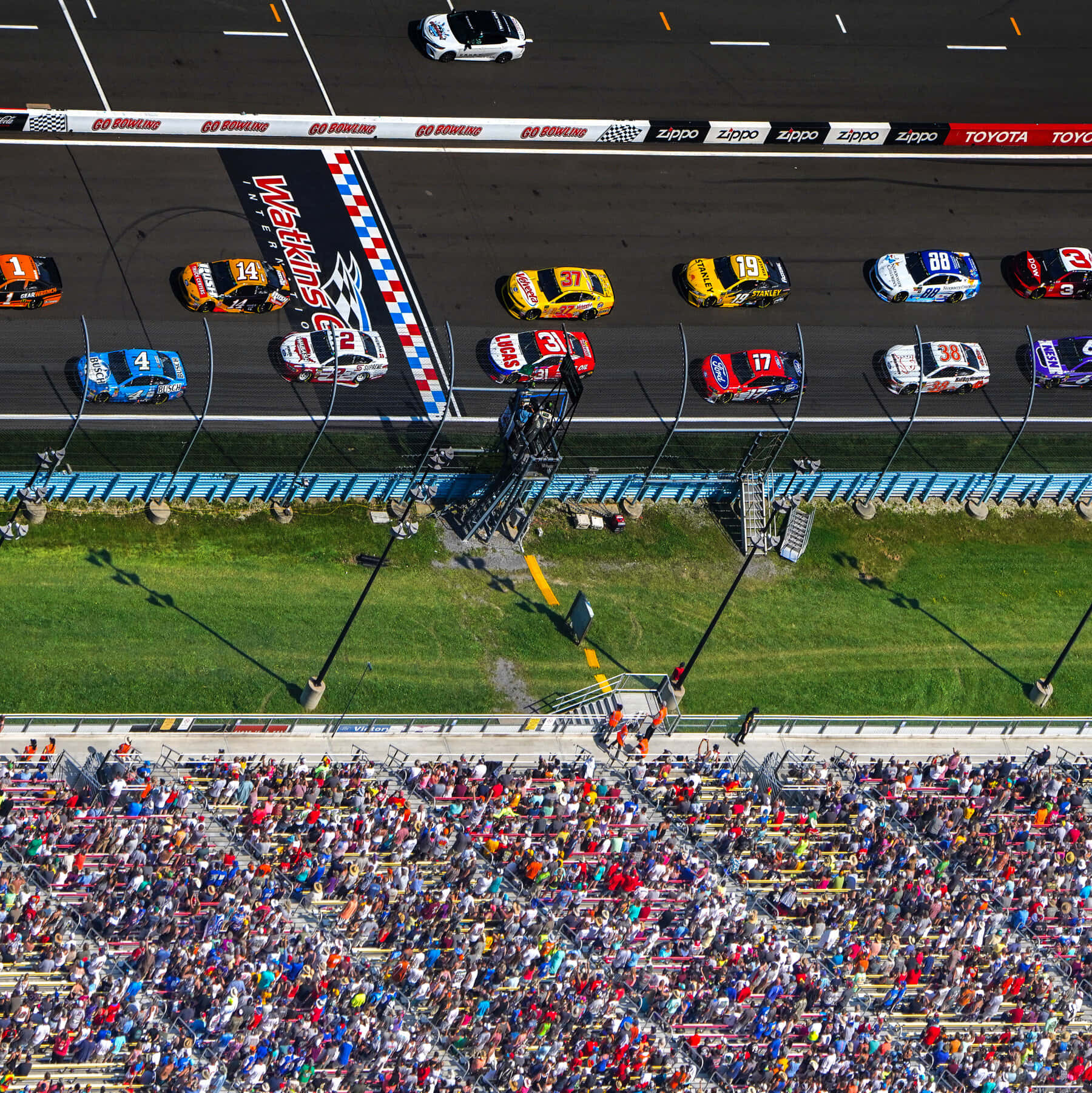 NASCAR賽事的刺激體驗 壁紙 — 從空中俯瞰馬丁斯維爾賽道，NASCAR賽車飛馳而過方格旗，下方擠滿了人群。