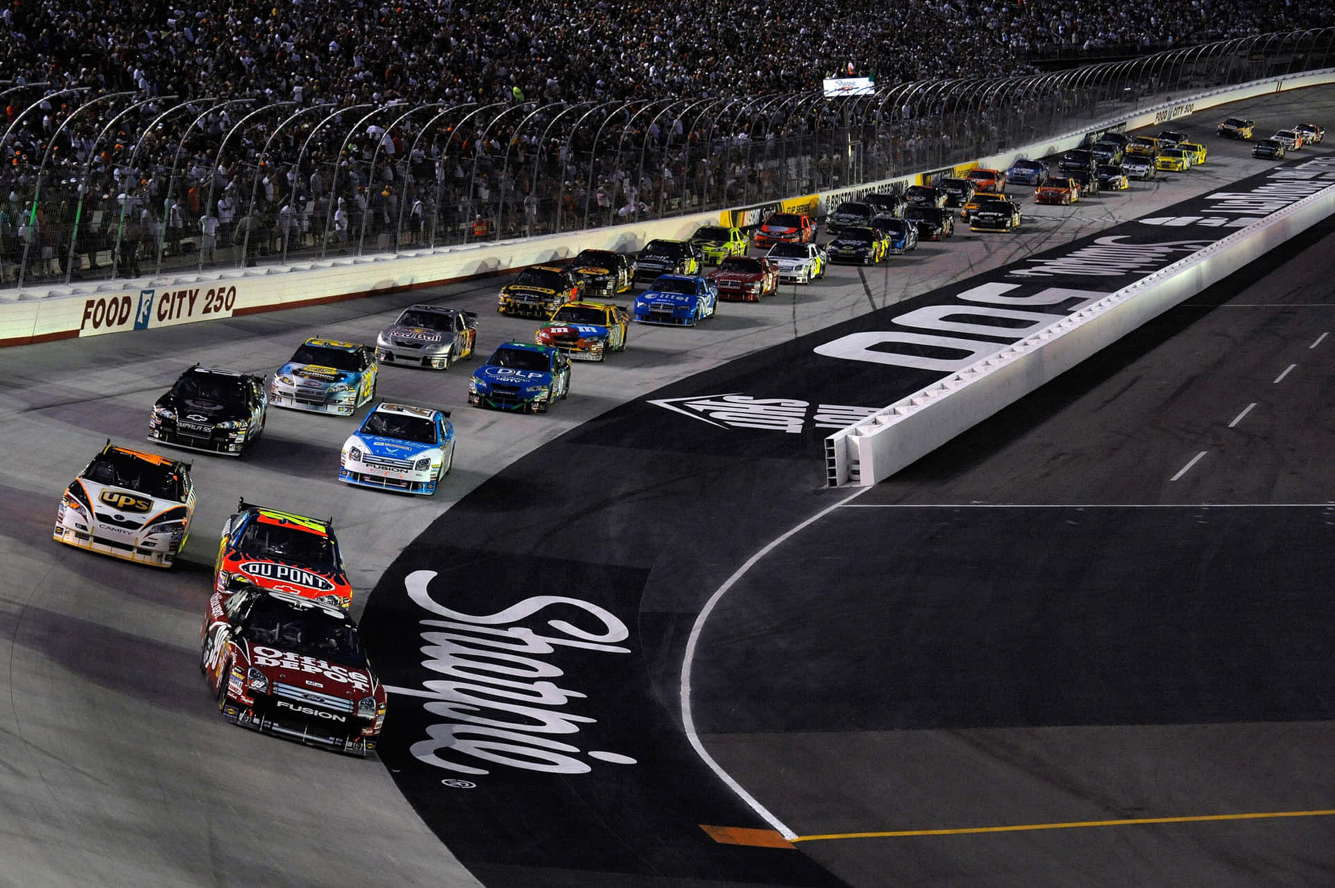 夜間NASCAR比賽，賽車在明亮燈光下於賽道上飛馳。