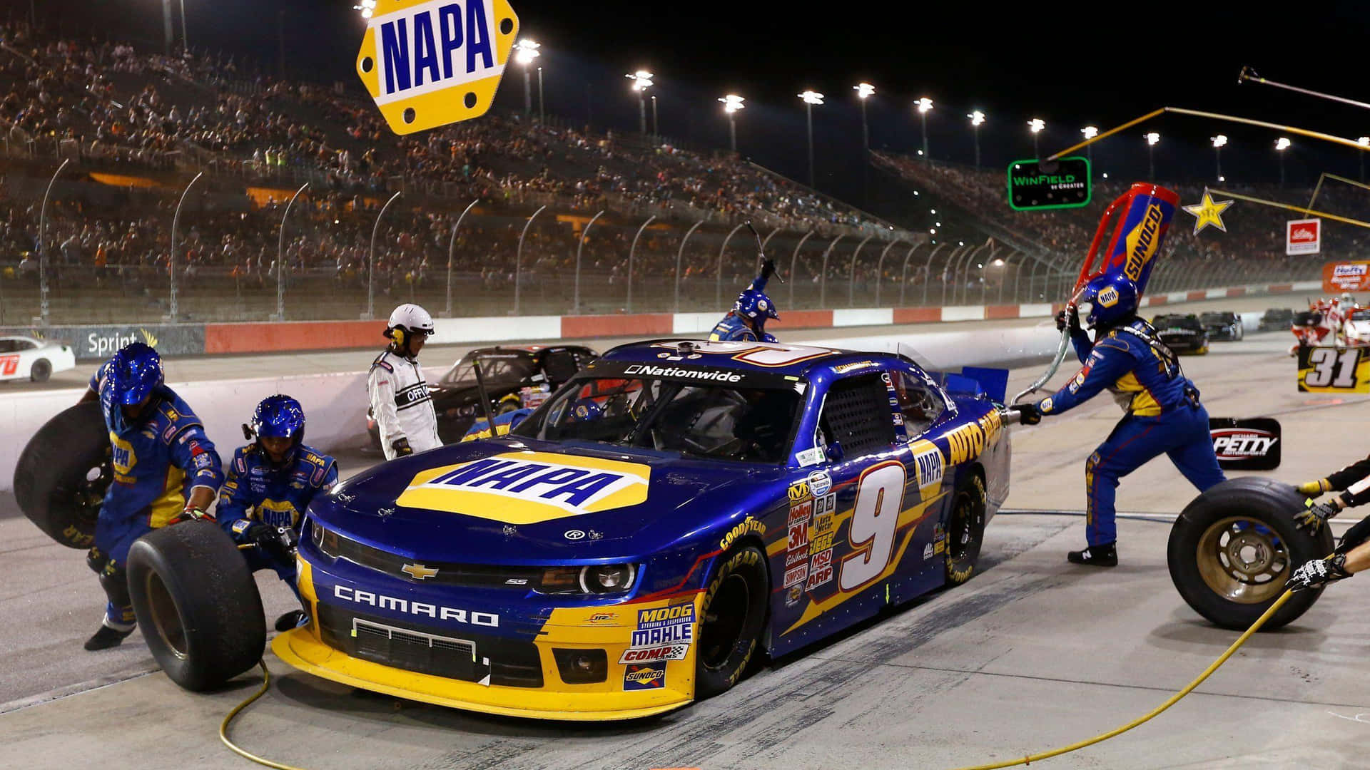 NASCAR維修站工作人員在夜間為一輛藍黃色賽車更換輪胎。