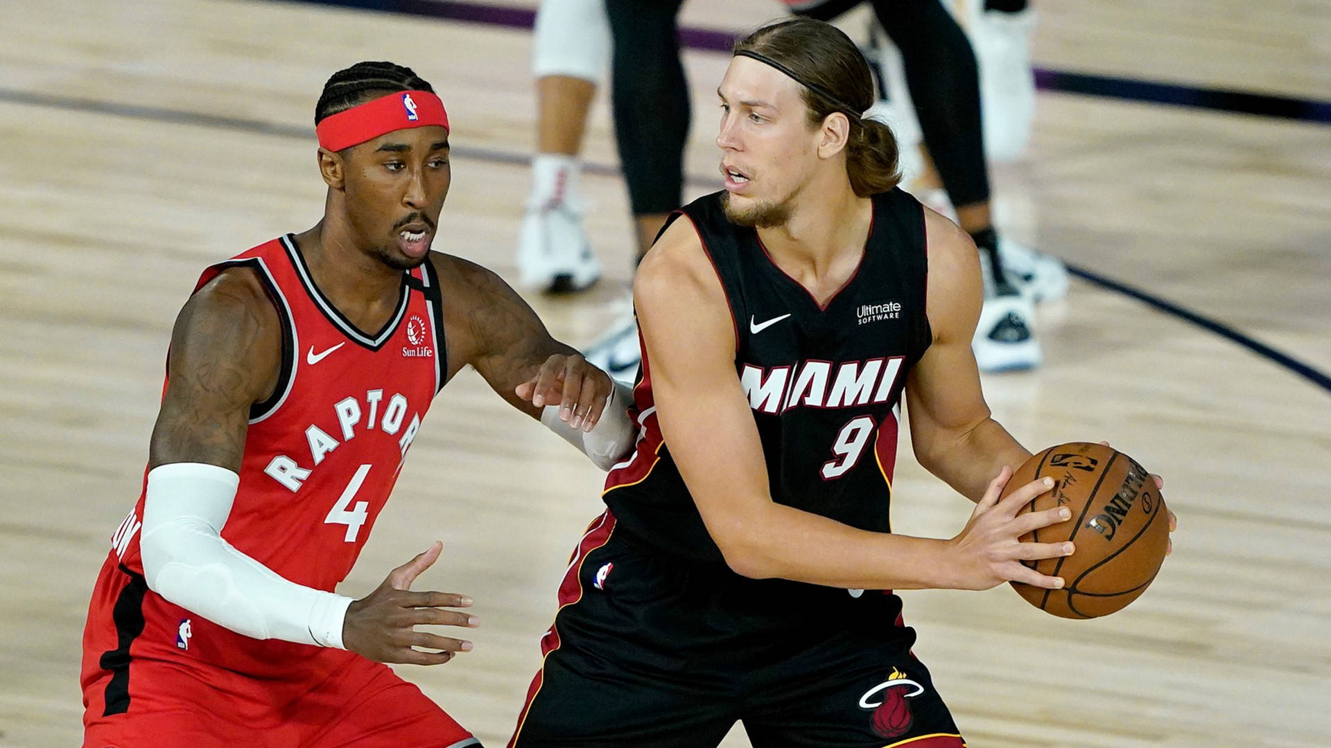 NBA總決賽猛龍對陣熱火 壁紙 — 兩名籃球運動員在硬木球場上激烈競爭，一人身穿紅色多倫多球衣，另一人身穿黑色邁阿密球衣，運球。