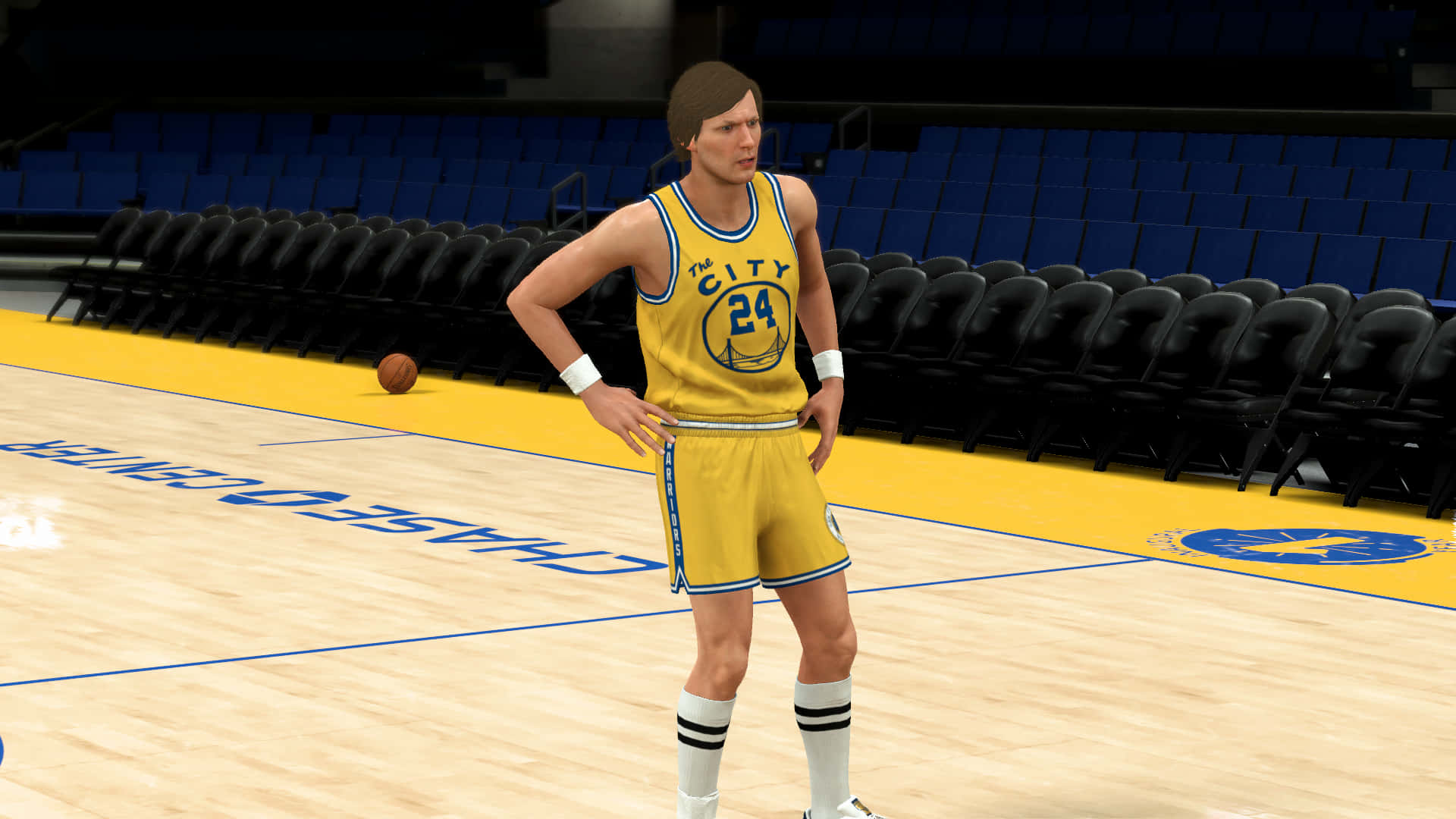 NBA 2K《The City》瑞克·巴里 球衣編號24 壁紙 — 一名身穿黃色'The City'球衣的籃球運動員自信地站在拋光球場上，身後是空無一人的藍色座位。