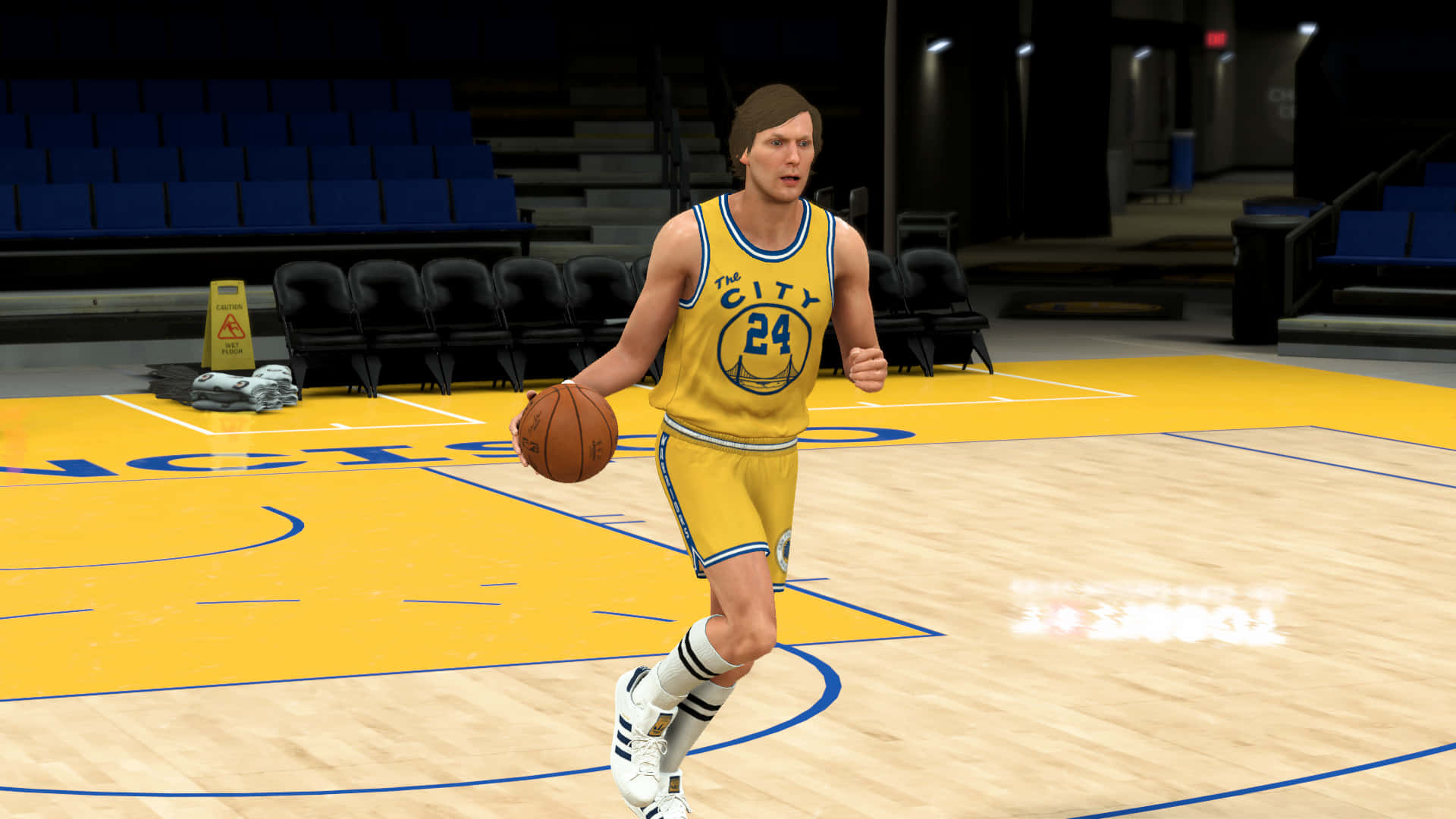 NBA 2K 舊金山戰士隊 瑞克·巴里 壁紙 — 一名身穿黃色 'The City 24' 球衣的籃球運動員在光線明亮的室內球場運球，背景是空無一人的藍色座位。
