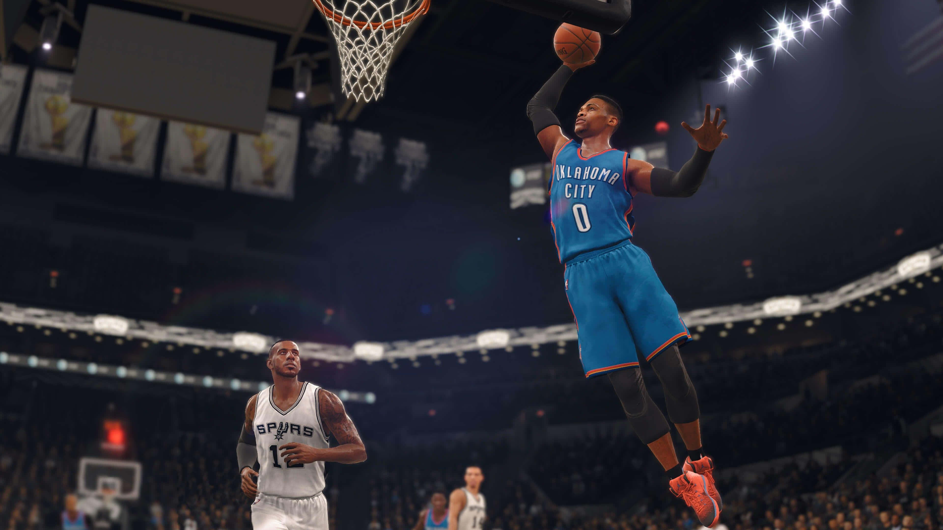 NBA 2K 魯斯·威斯布魯克 壁紙 — 一名身穿藍色奧克拉荷馬城球衣的籃球運動員正在入樽，而一名馬刺球員在擠滿觀眾的場館下方觀看。