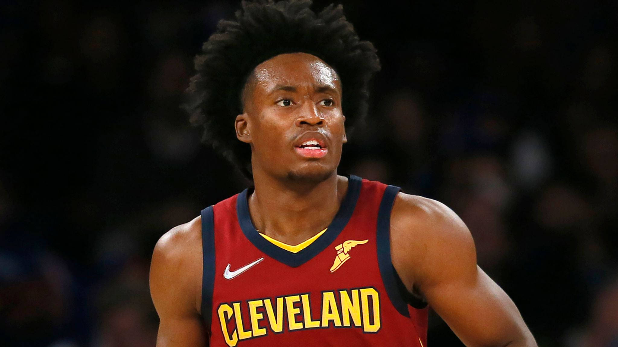 NBA 2號球員科林·塞克森 壁紙 — 一名專注的籃球運動員身穿紅色克里夫蘭球衣，帶有黃色字體和標誌，在明亮的場館燈光下比賽時專注地向前凝視。