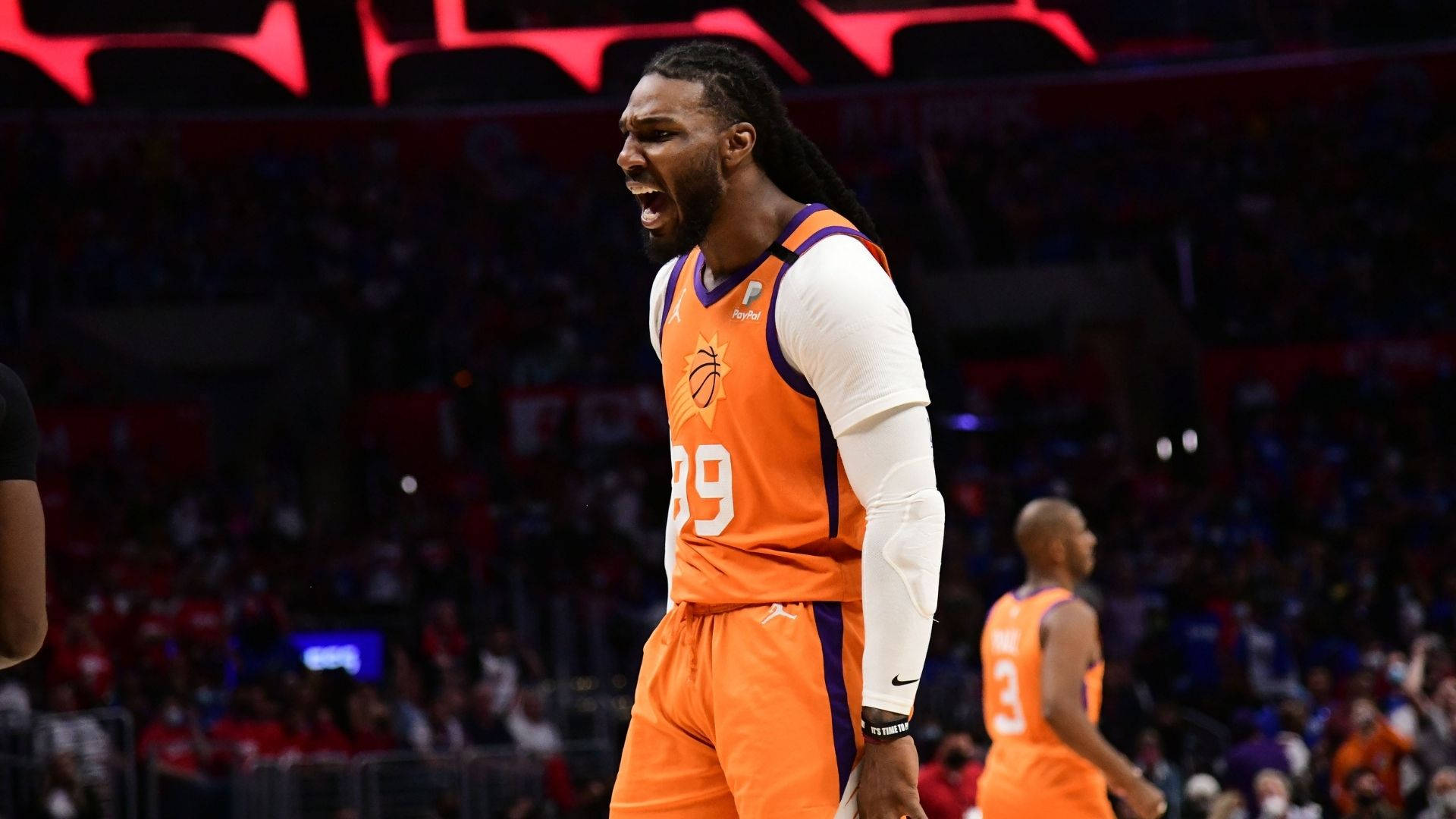 NBA總決賽賈伊·克勞德怒吼 壁紙 — 一名身穿橙色球衣的籃球運動員在明亮的場館燈光下，在比賽中激烈咆哮。
