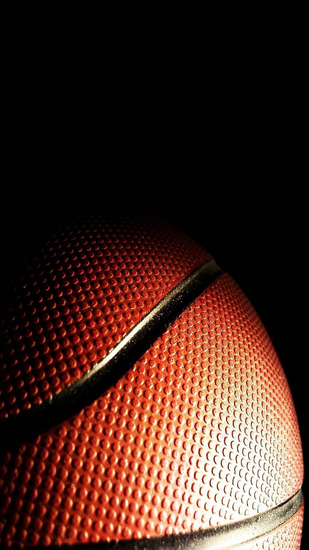 NBA iPhone 影子中的籃球 壁紙 — 一個紋理橙色籃球的特寫，在黑色背景下被戲劇性的燈光照亮。