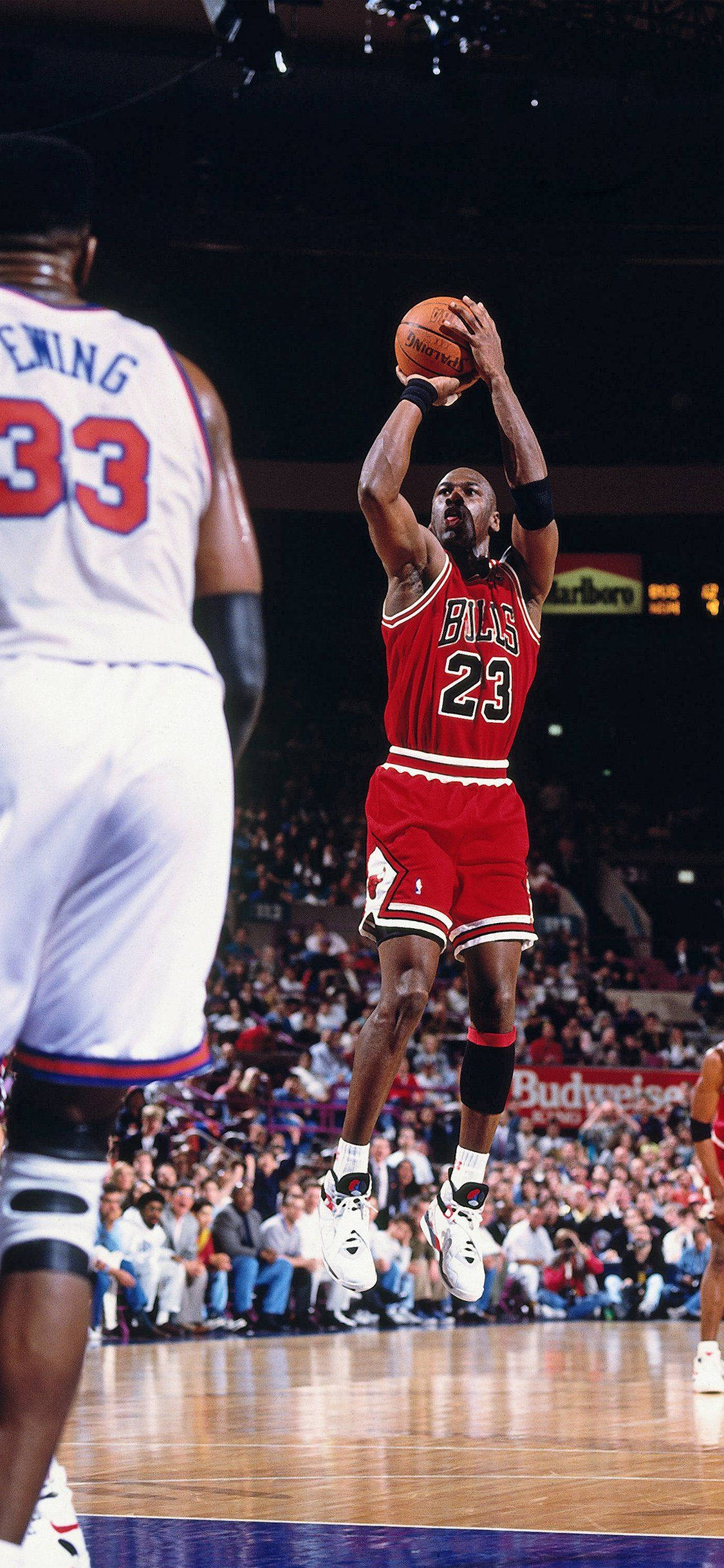 NBA iPhone 傳奇人物邁克爾·喬丹 壁紙 — 米高佐敦身穿紅色公牛隊球衣，在擠滿觀眾的場館中高高躍起，越過防守球員投出致勝一球。