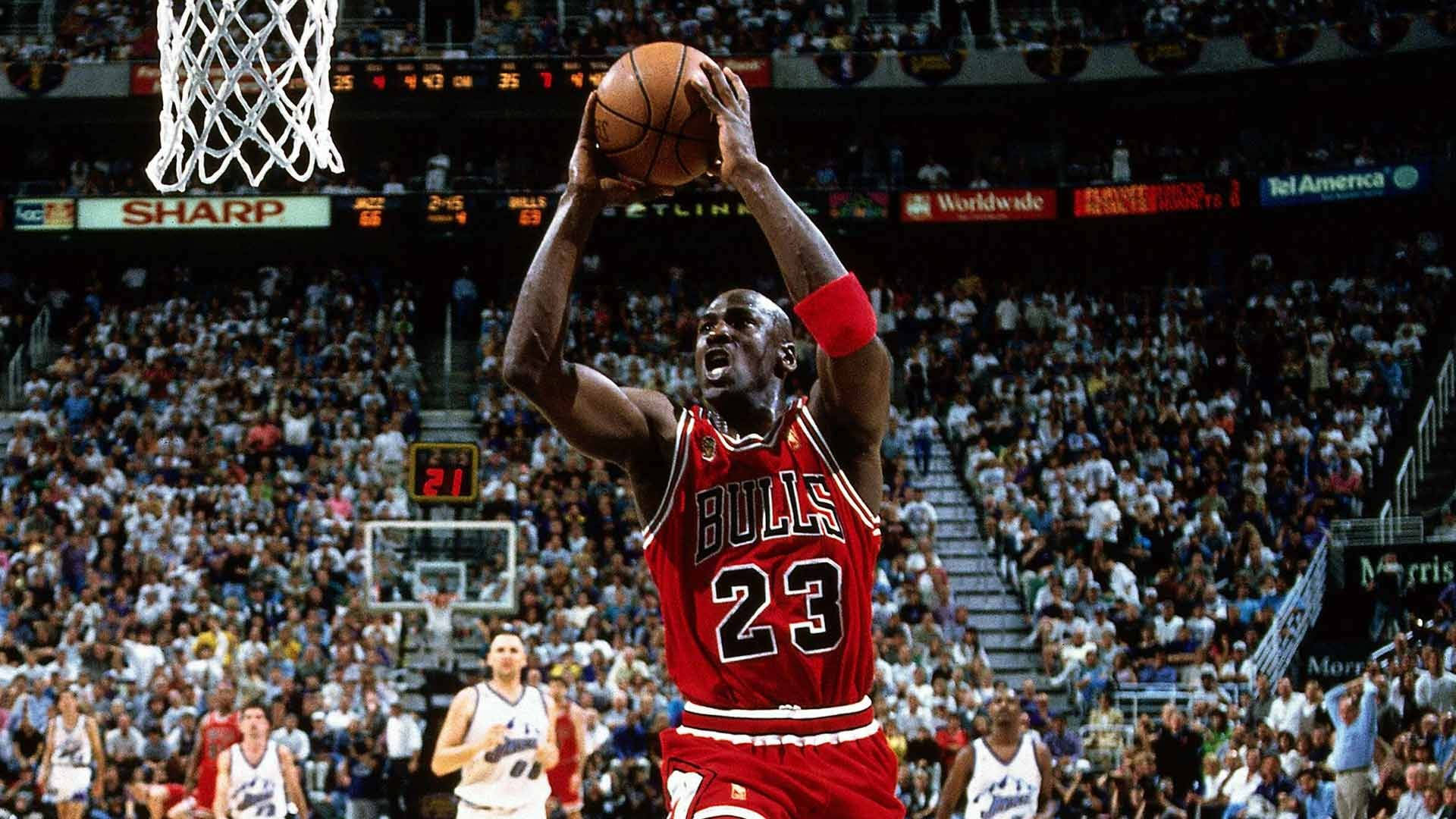 NBA總決賽精彩時刻 壁紙 — 米高佐敦身穿紅色公牛隊球衣，在明亮的場館燈光下，於座無虛席的場館中跳起入樽。