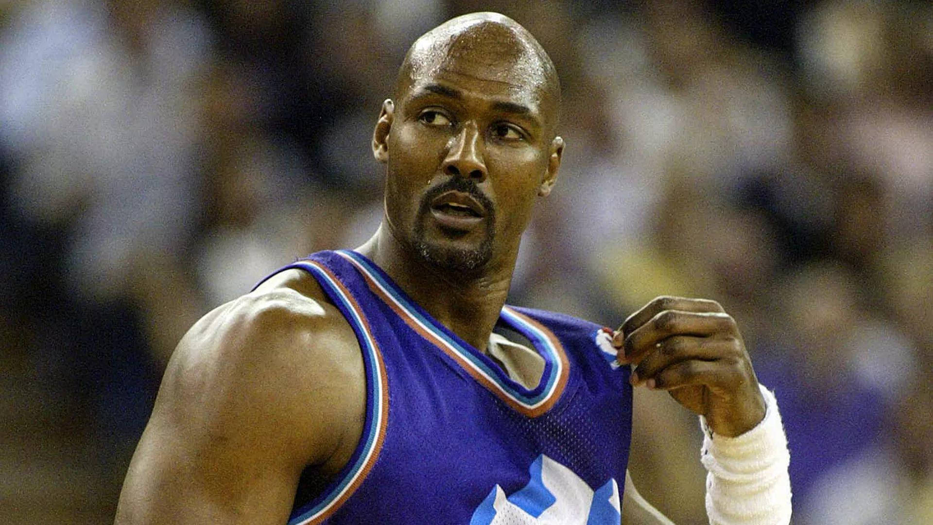 NBA傳奇球星卡爾·馬龍 壁紙 — 一位身穿紫色球衣的專注籃球運動員在明亮的場館燈光下，於激烈的比賽中緊握他的護腕。