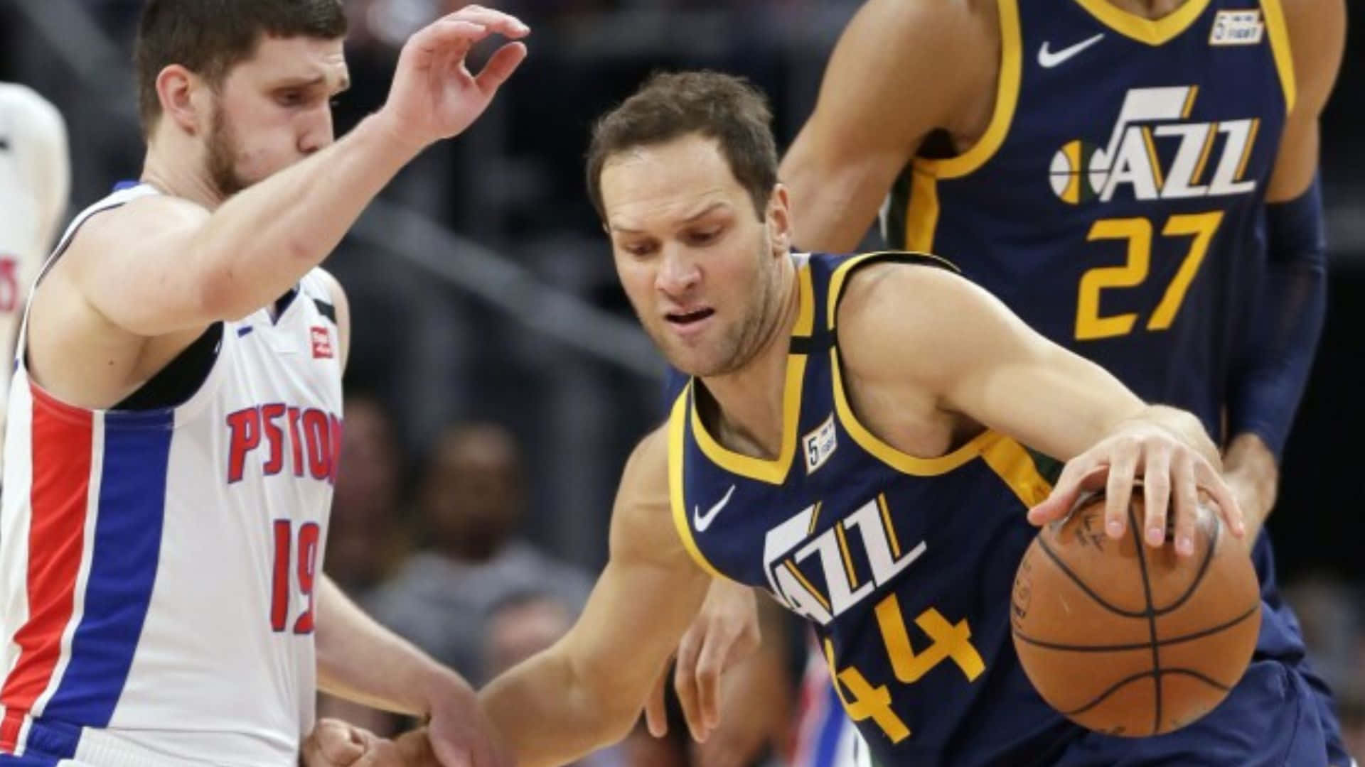 NBA 博揚·博格達諾維奇 球衣編號44 壁紙 — 一名身穿藍色和金色球衣的猶他爵士隊球員運球，同時被一名身穿白、紅、藍色的底特律活塞隊球員緊密防守。