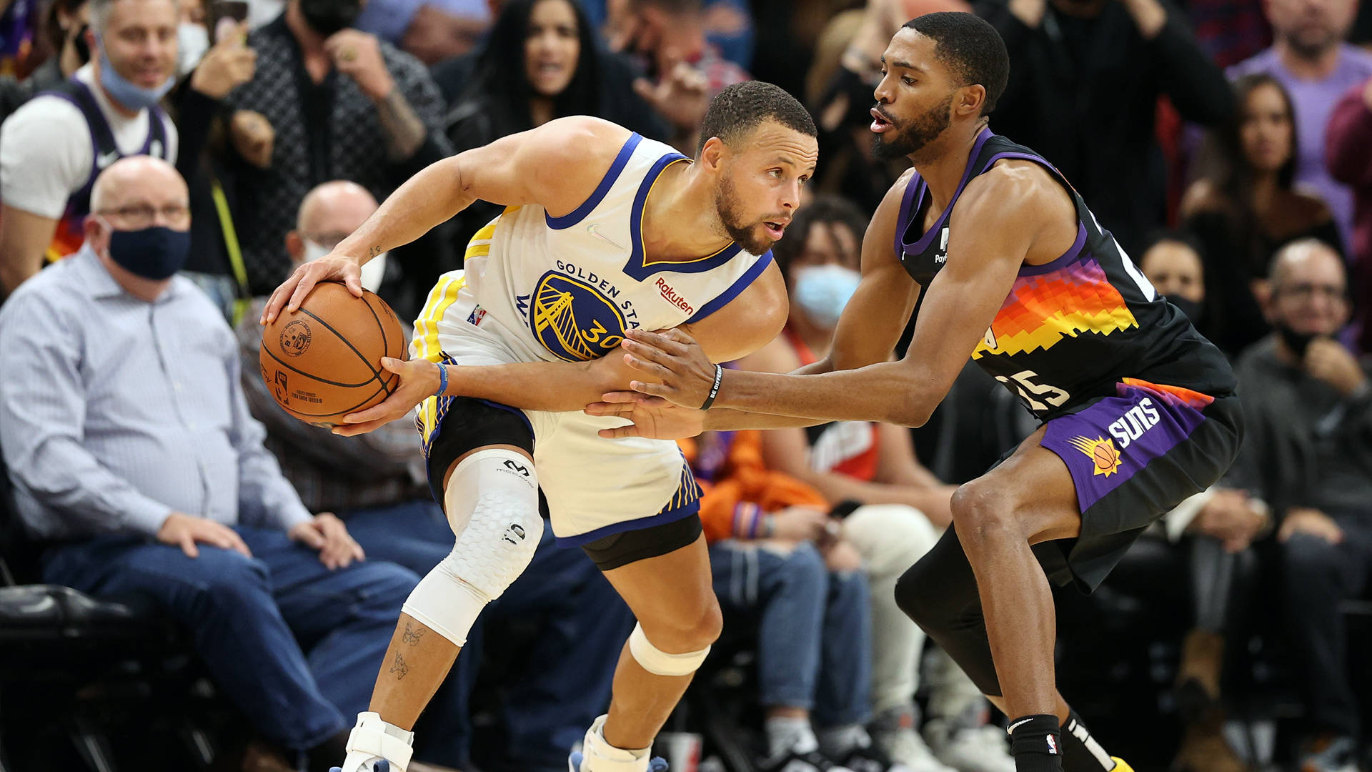 NBA 後衛 米卡爾·布里奇斯 壁紙 — 一名身穿白色金州勇士隊球衣的籃球運動員在激烈的比賽中帶球突破鳳凰城太陽隊的防守球員。